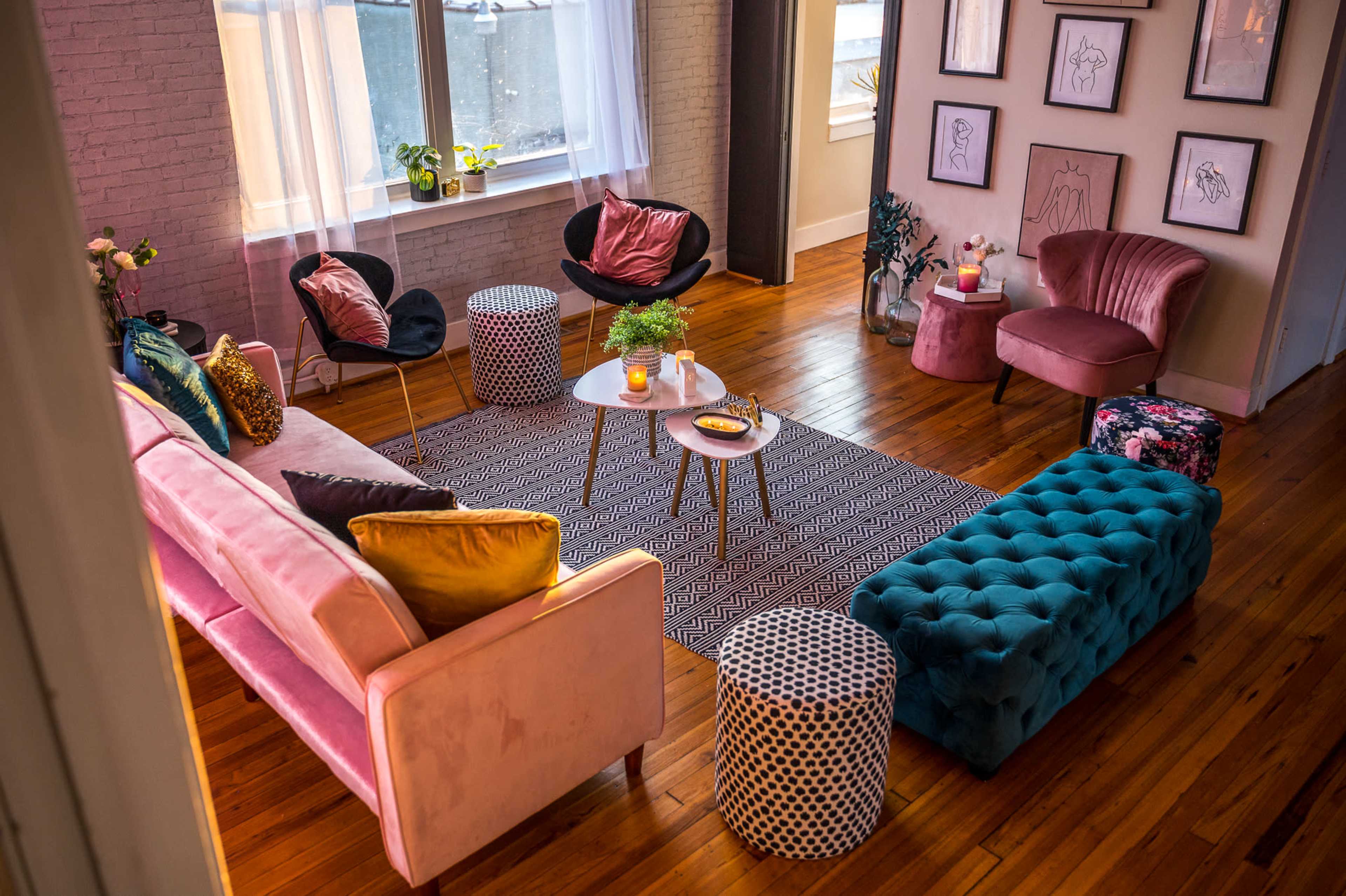 A cozy living room features a mix of seating options, including a pink sofa, black chairs, and various accent tables arranged around a patterned area rug.
