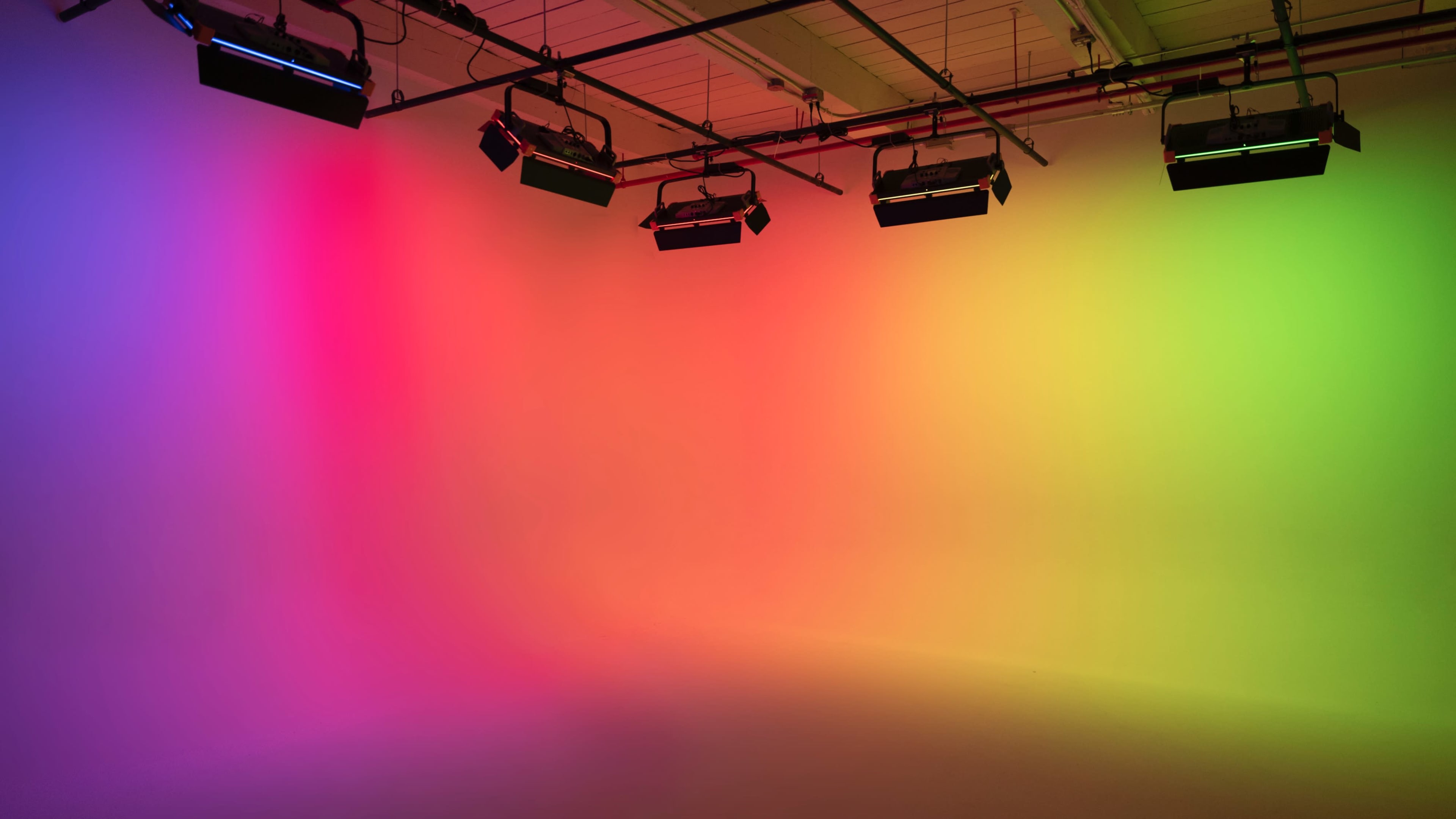 A studio room features a gradient background illuminated by multiple colored lights.