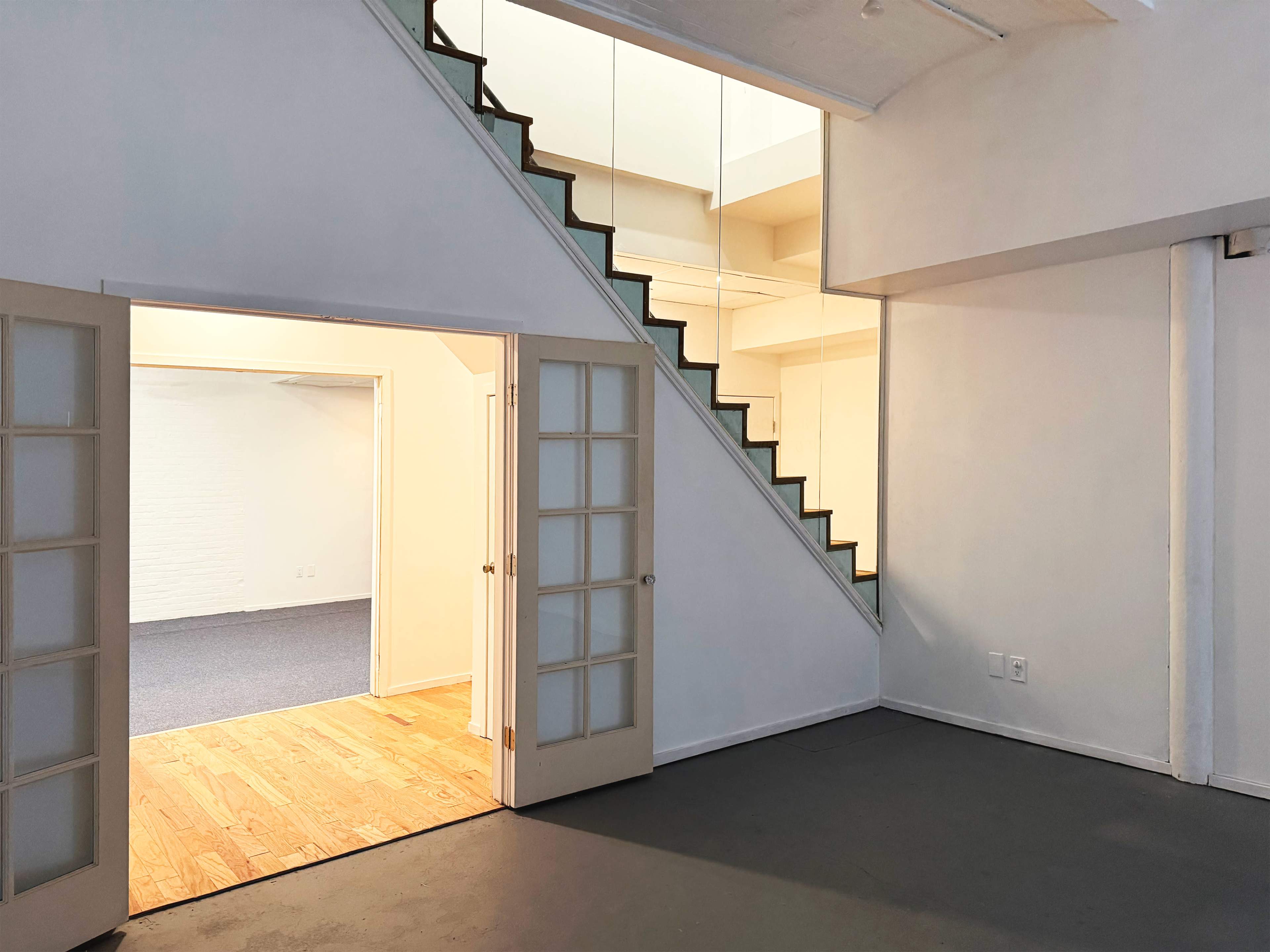 The image shows a modern interior space with a staircase leading to a second level and a doorway that opens into a second room.