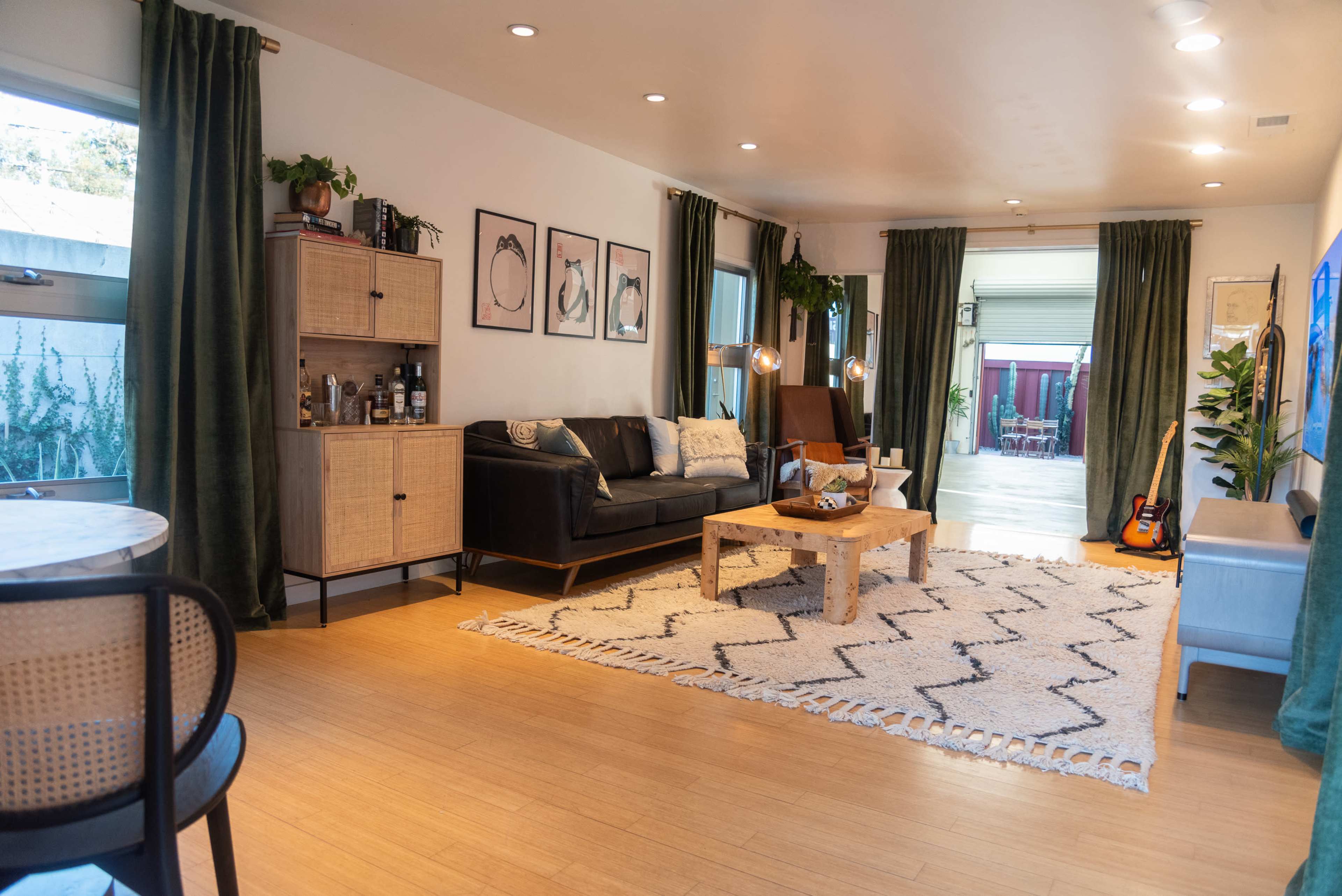 The image shows a modern living room with a large rug, a black leather sofa, a coffee table, and artwork on the walls.