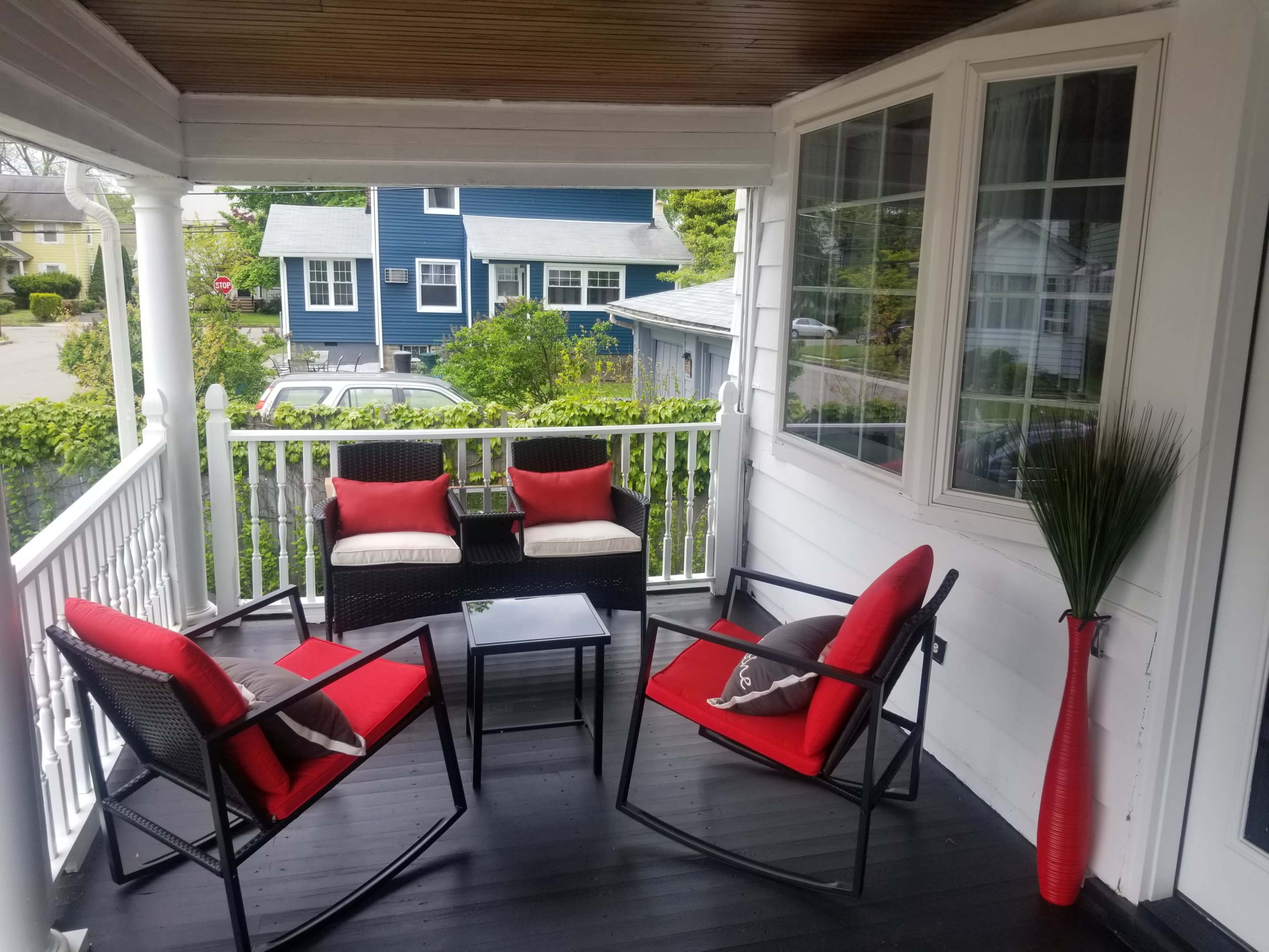 A porch features two chairs and a small table, all arranged around a decorative plant.