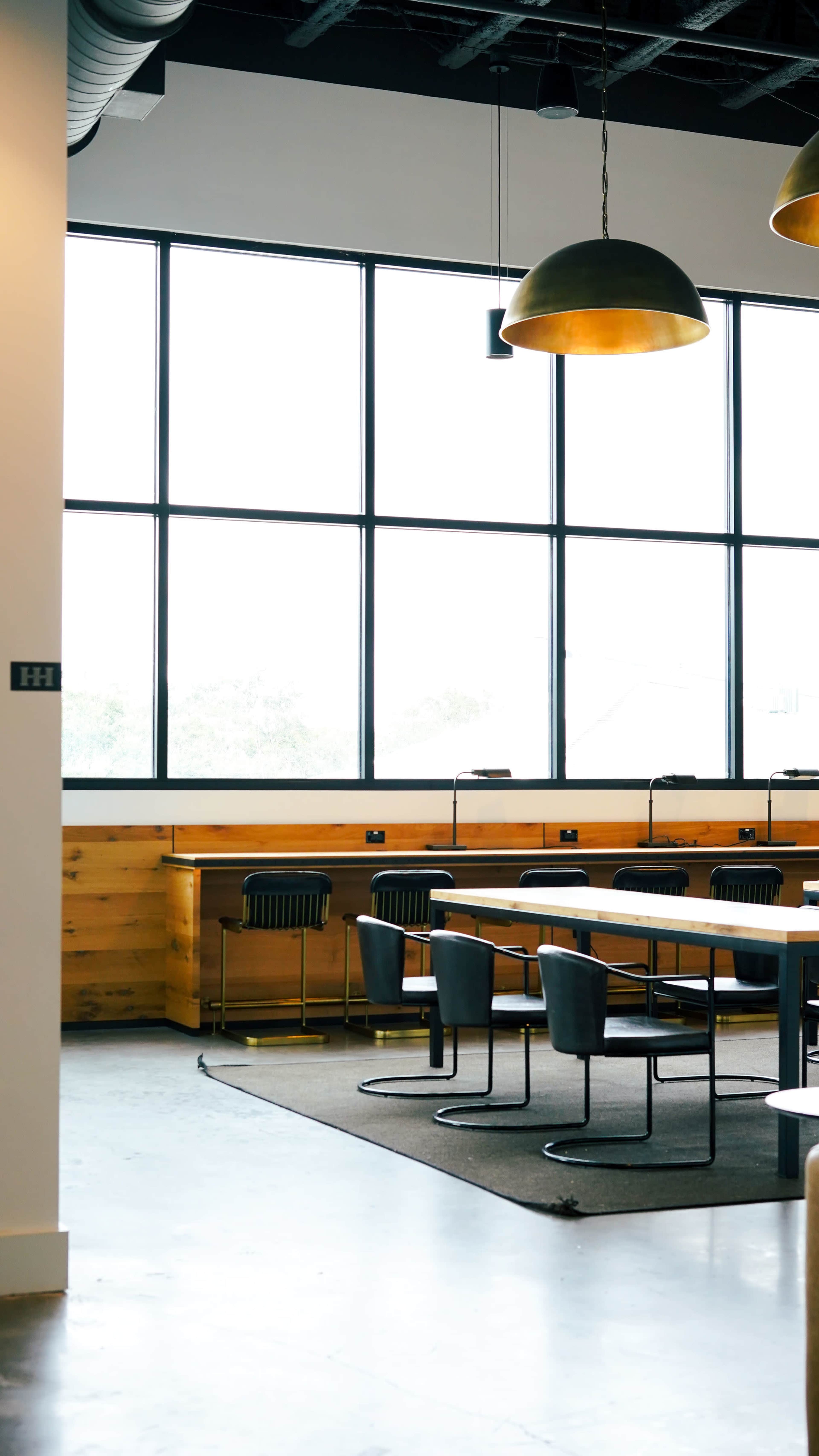 The image shows a modern, spacious interior with large windows, featuring a table surrounded by chairs and a counter with bar seating.
