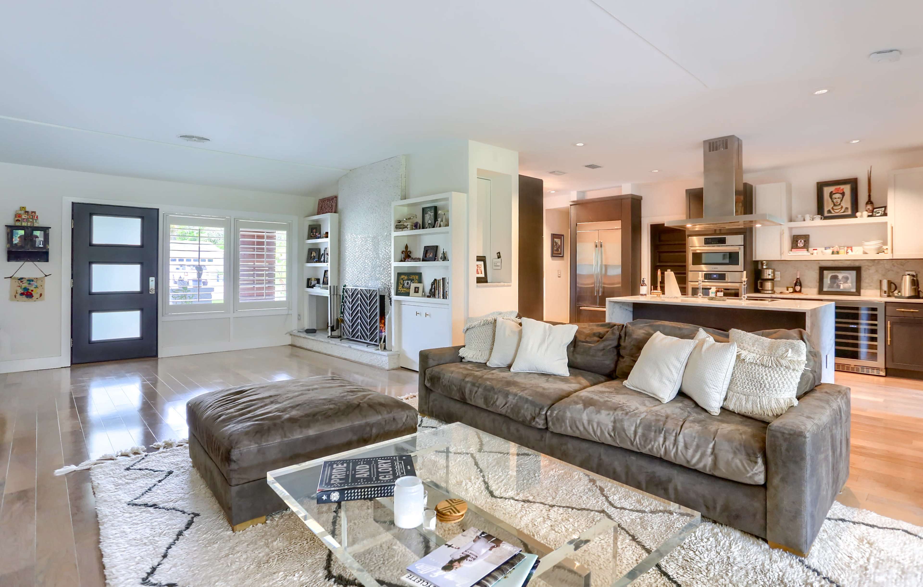 A spacious living room with a large sofa, a glass coffee table, and an open kitchen area in the background.