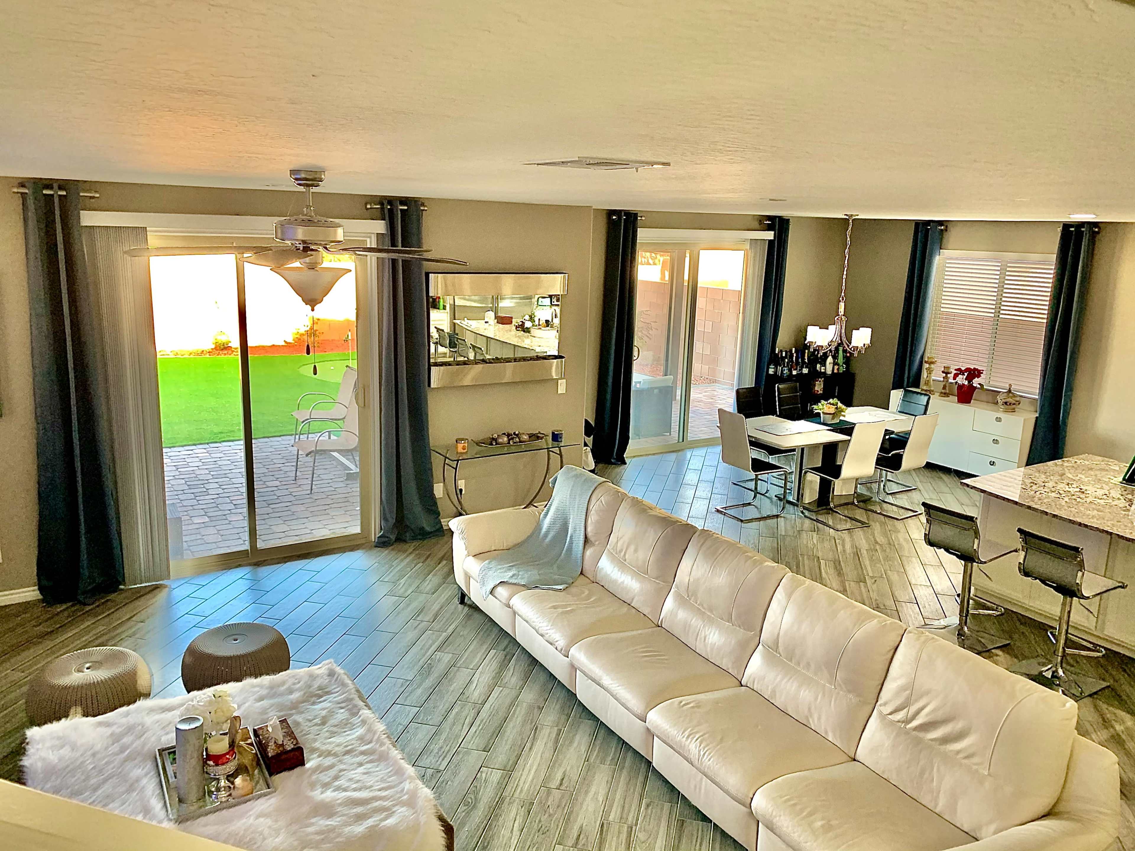 The image features a modern living space with a white sofa, a dining area, and large glass doors leading to a backyard.