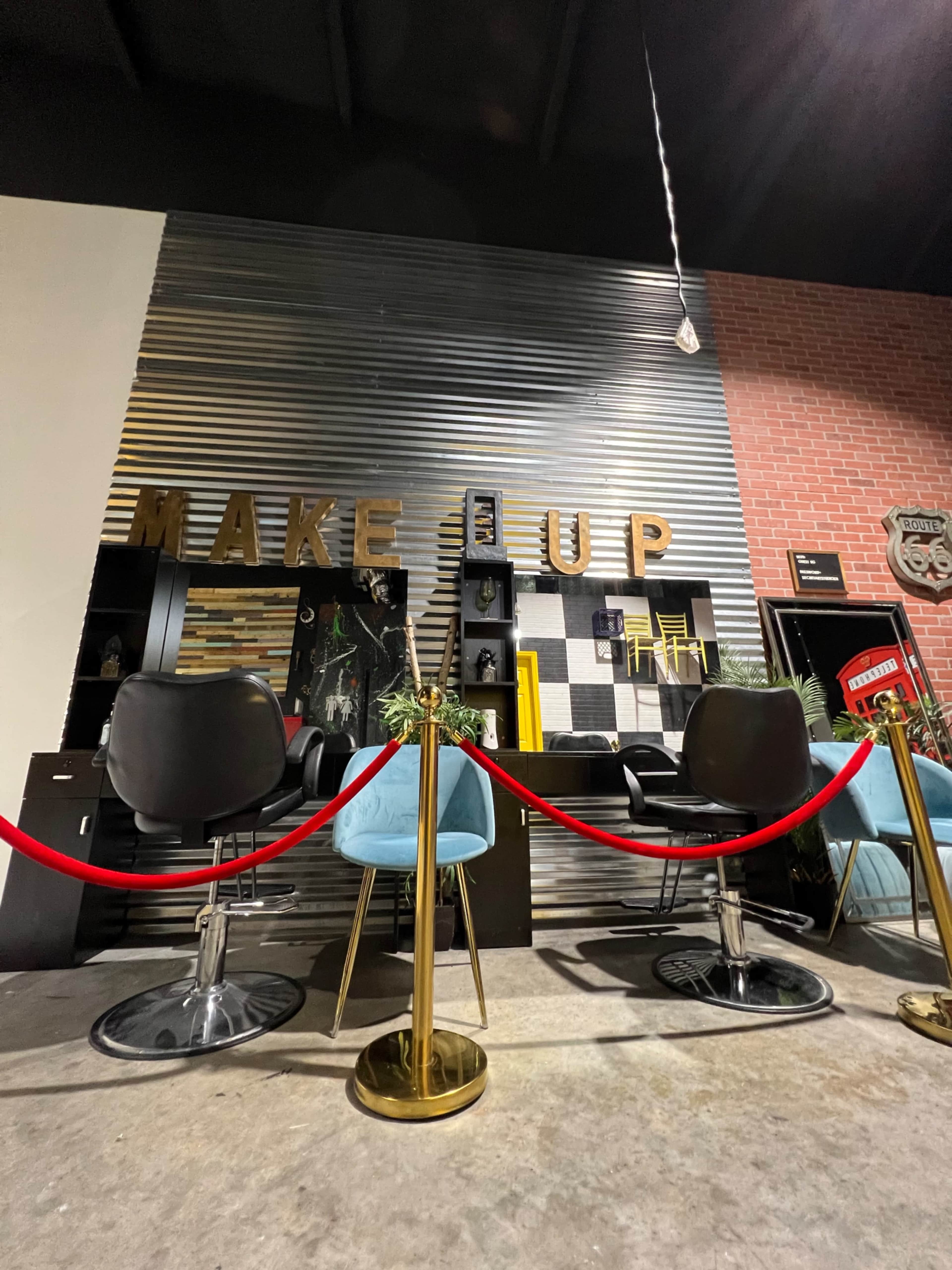 The image shows a modern makeup display area with chairs, a counter, and decorative elements, surrounded by a red rope barrier.