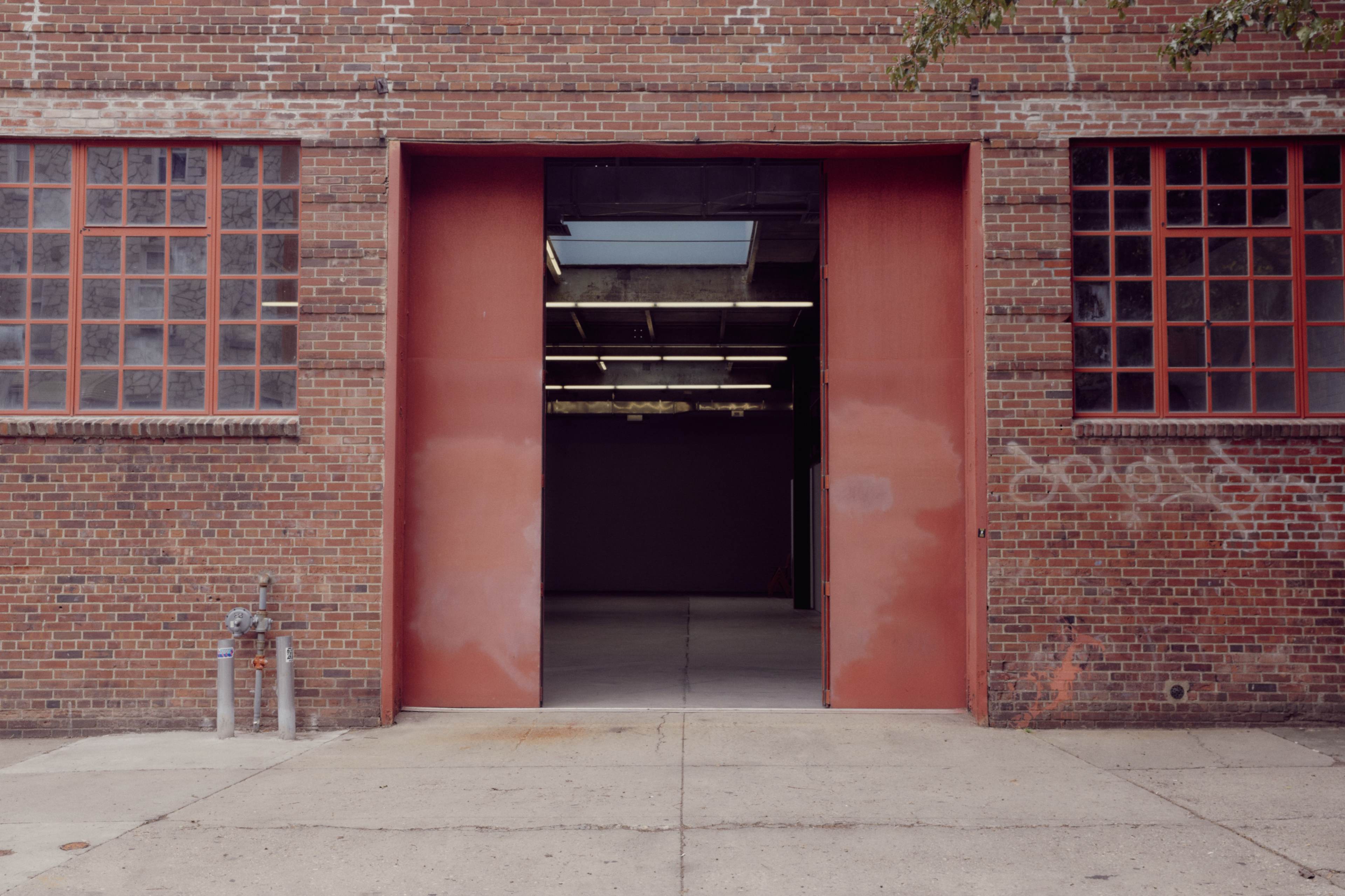 A large, red double door leads into an empty, industrial space within a brick building.