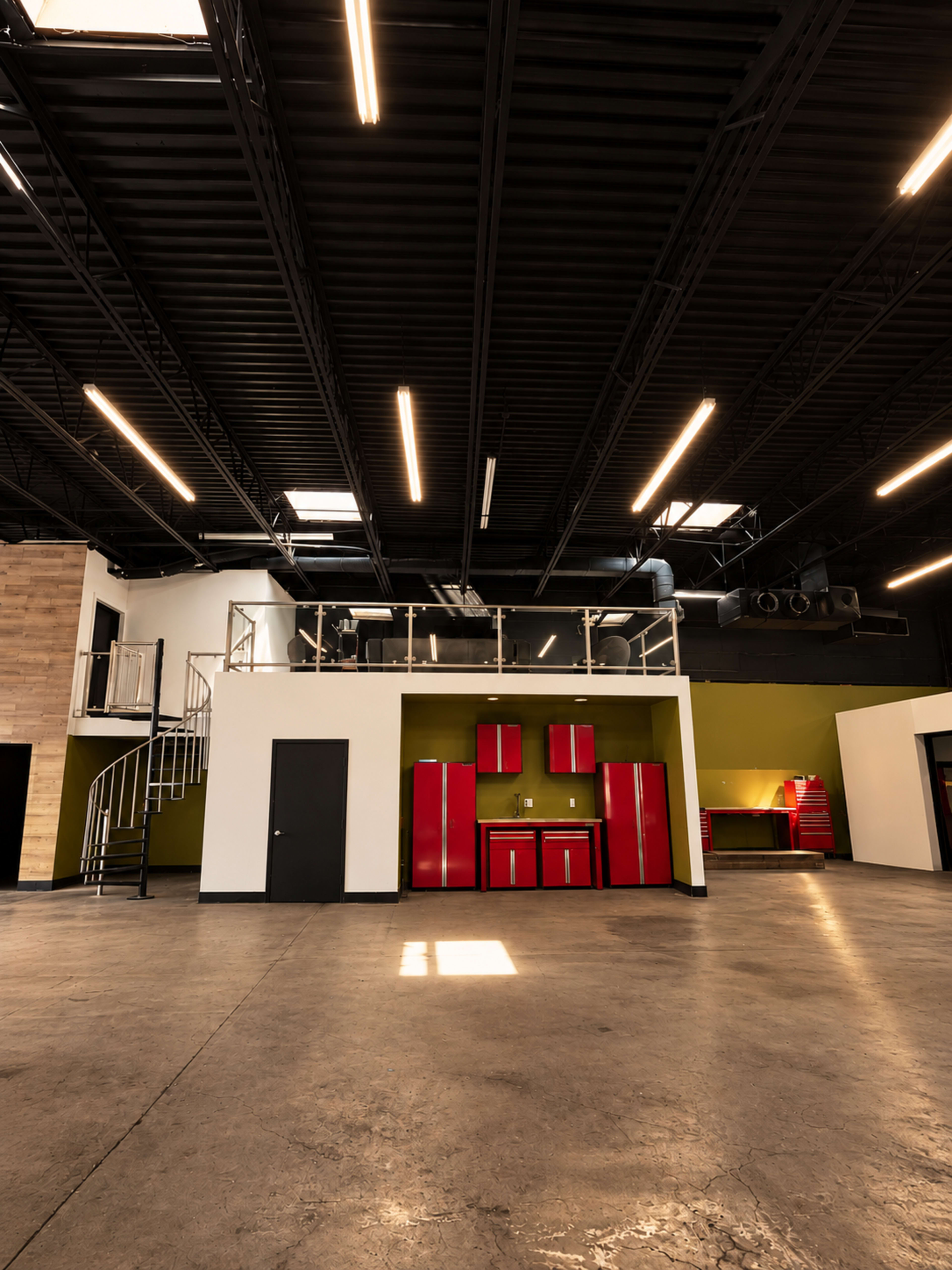 The image shows a spacious interior of an industrial-style building featuring a kitchen area with red cabinets and a spiral staircase leading to an upper level.