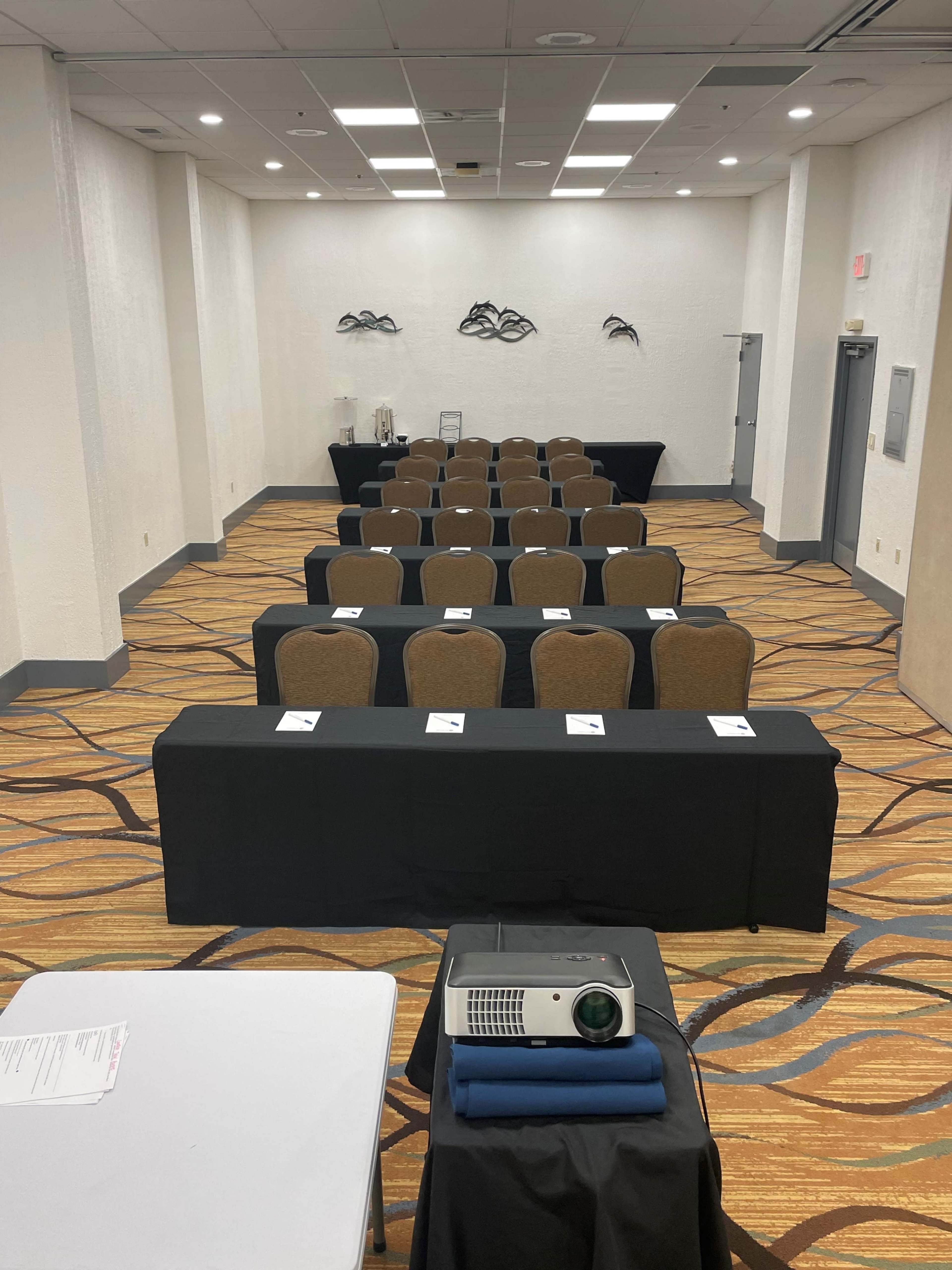 A conference room set up with rows of tables and chairs, a projector on a table at the front, and name cards placed at each seat.