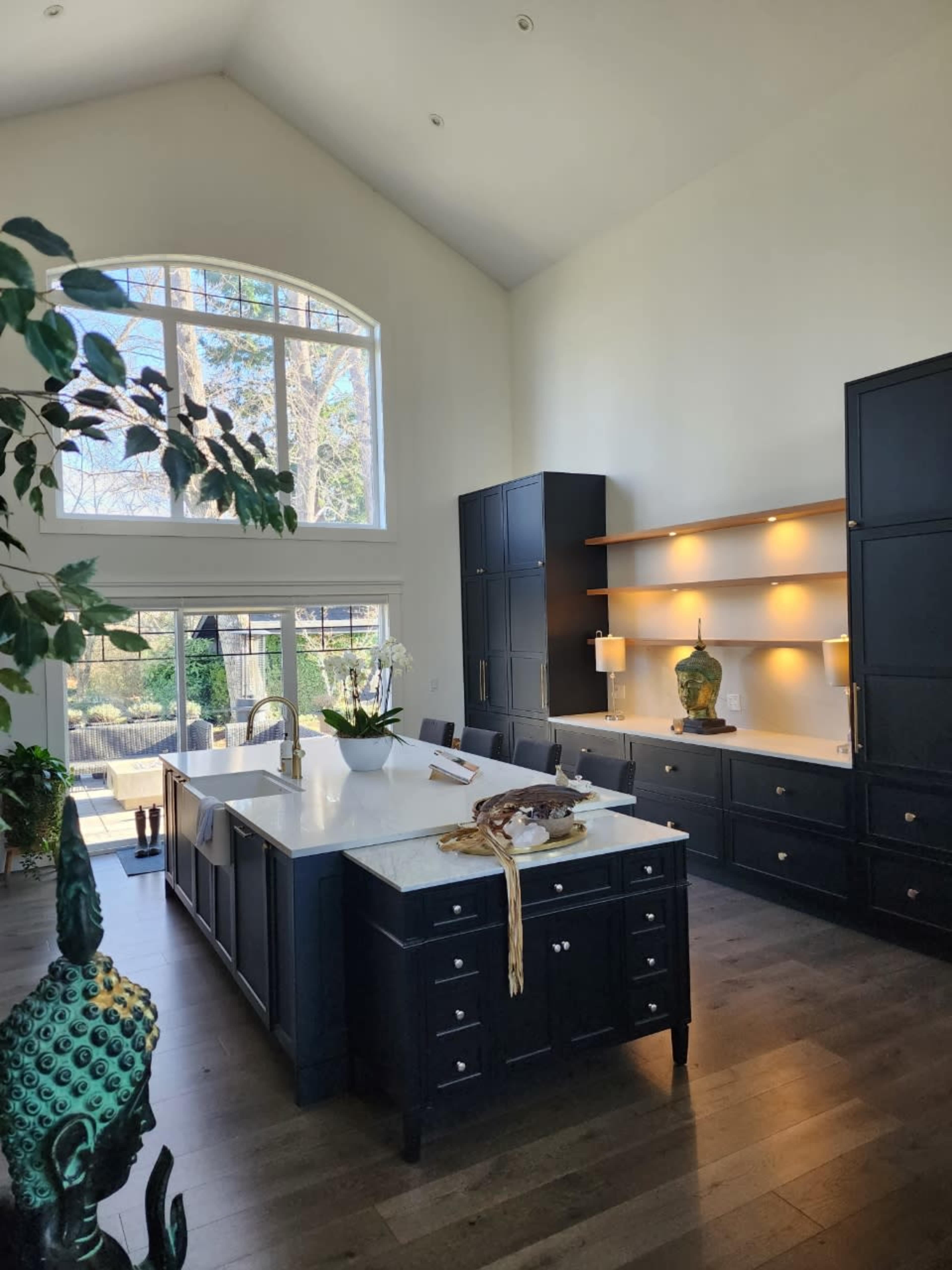 The kitchen features a central island with a marble countertop, dark cabinetry, and large windows that allow natural light to fill the space.