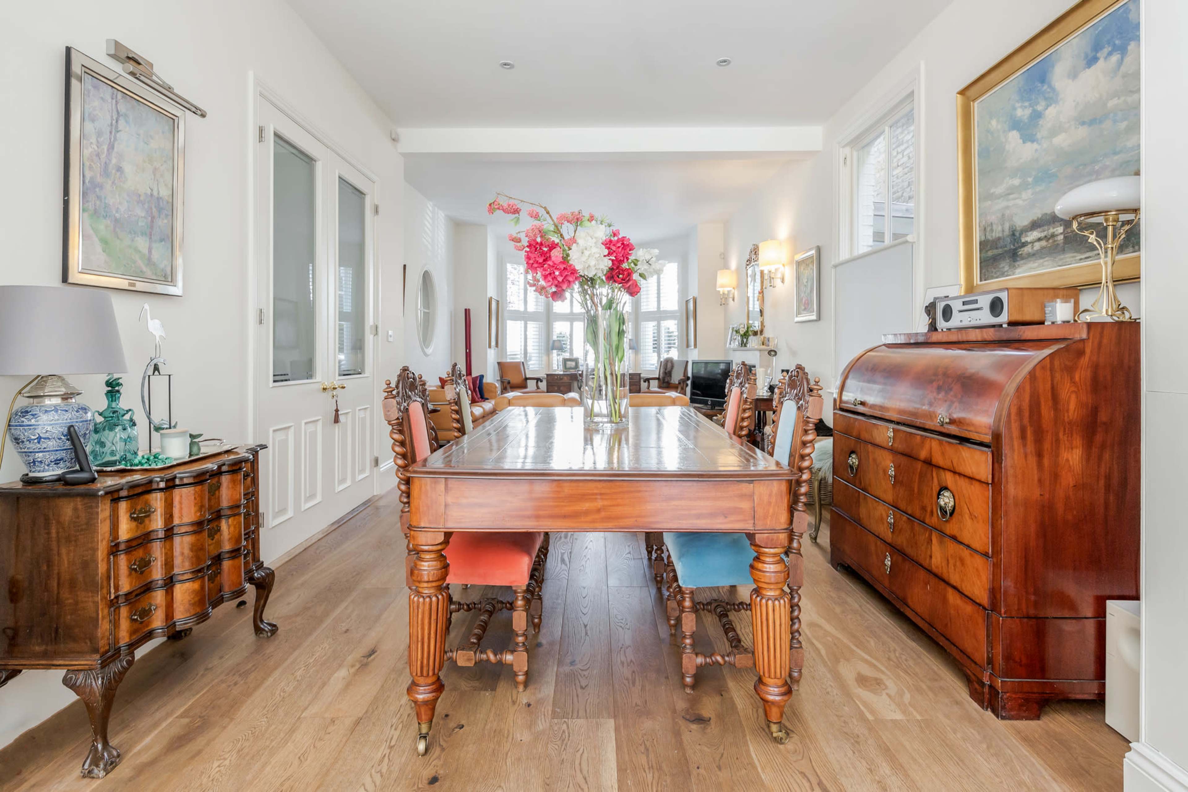 A spacious dining area with a wooden table, chairs with colored upholstery, and decorative furniture pieces along the walls.