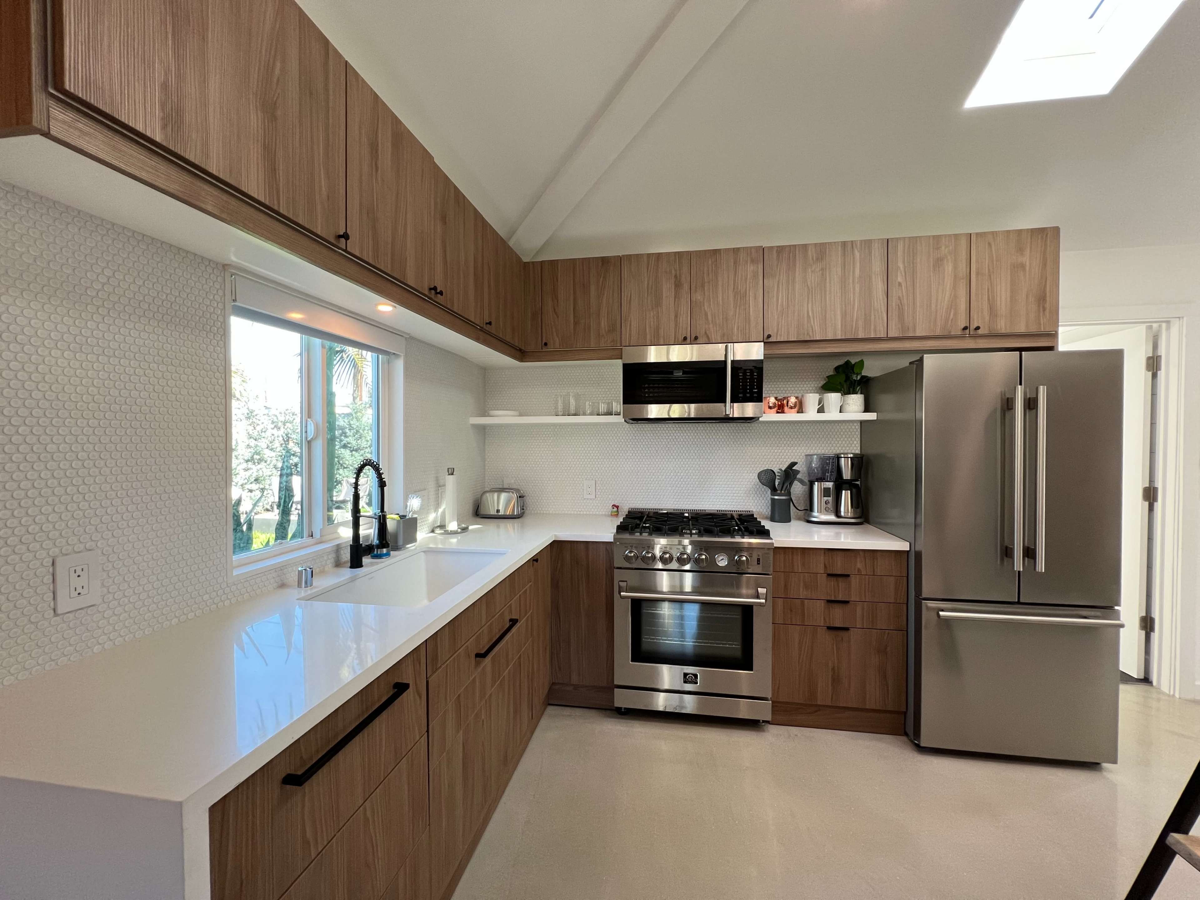 This kitchen features a modern design with wooden cabinetry, stainless steel appliances, a large sink, and ample natural light from a window.