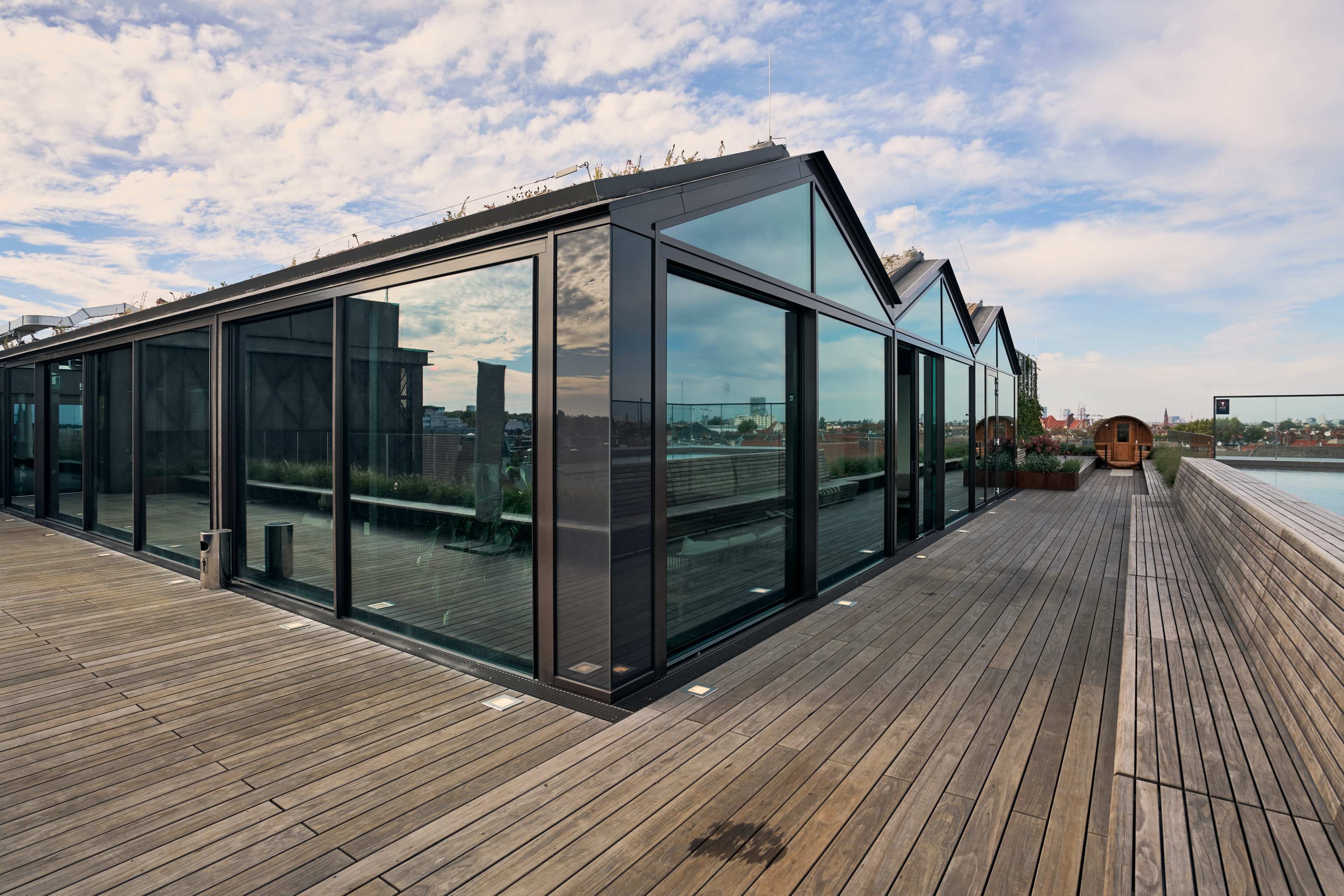 The image shows a modern building with large glass windows and a wooden deck area, set against a backdrop of a cloudy sky.