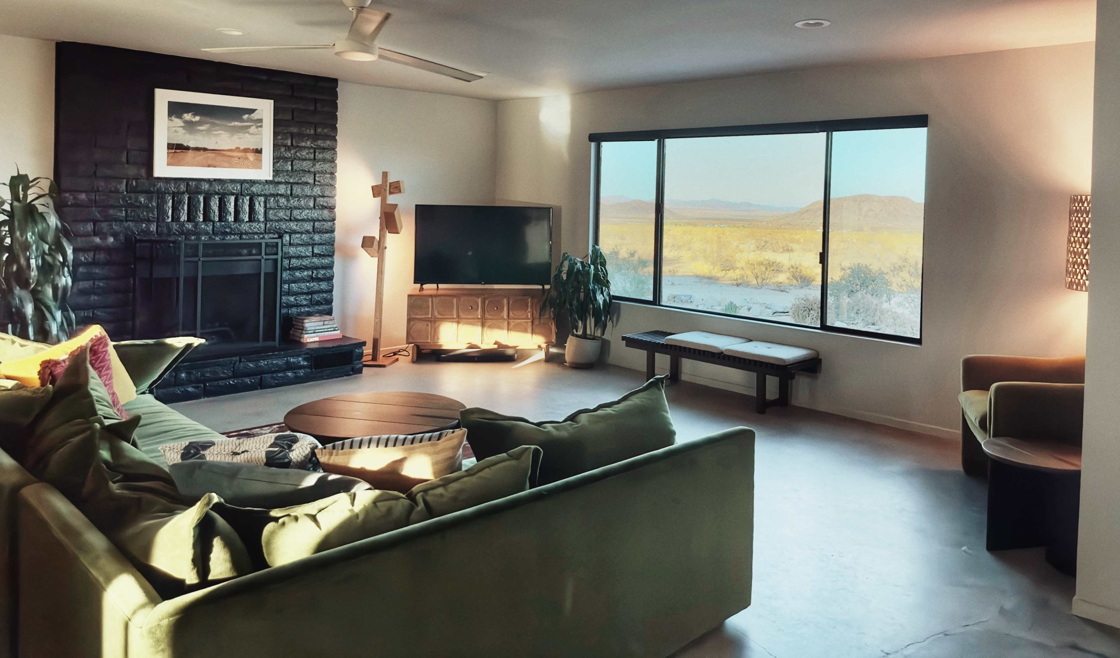 A living room features a green sectional sofa, a black stone fireplace, a television, and large windows overlooking a desert landscape.