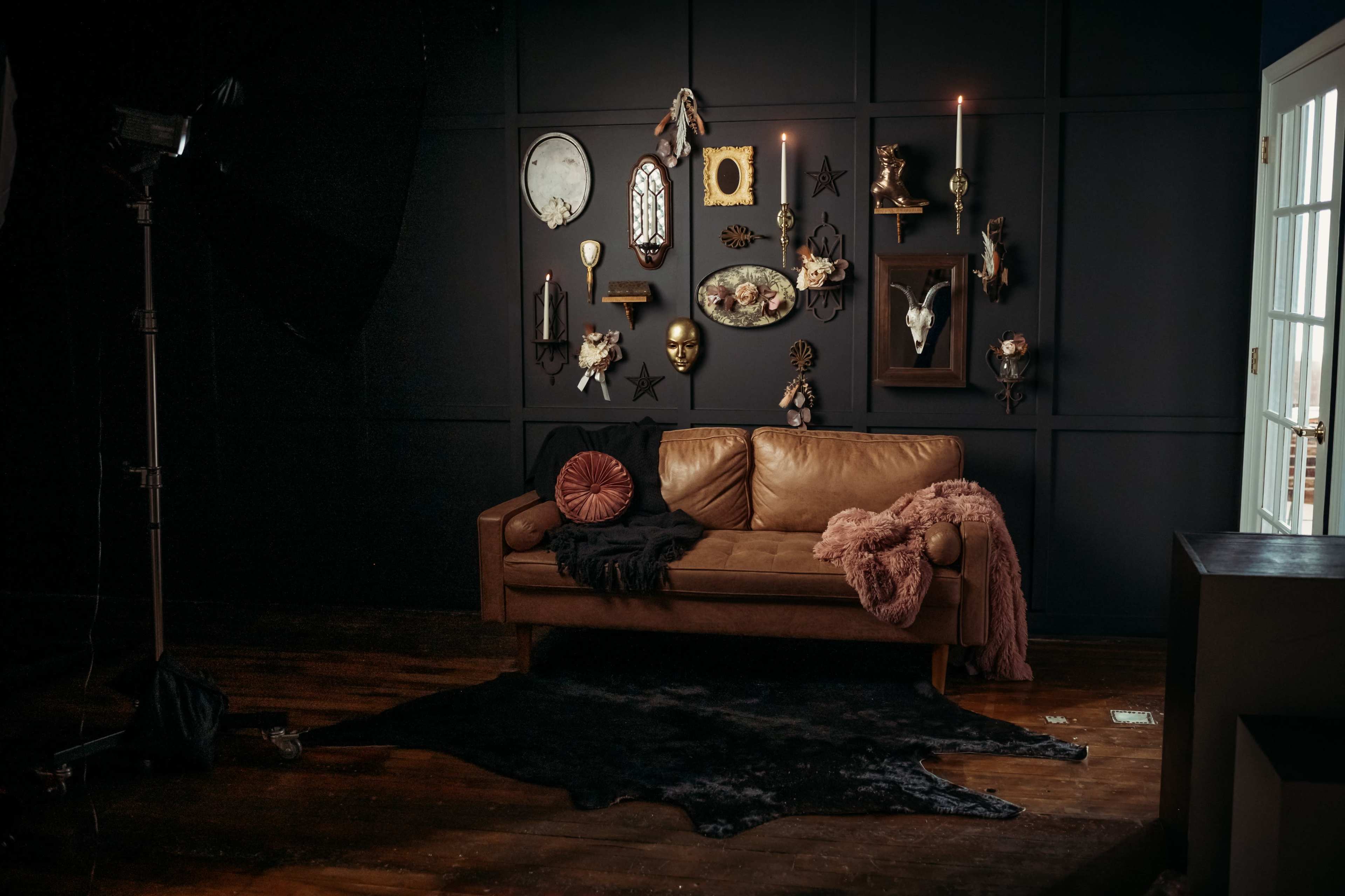 A leather sofa is positioned against a dark wall adorned with various decorative objects and framed art, while a rug lies on the wooden floor.