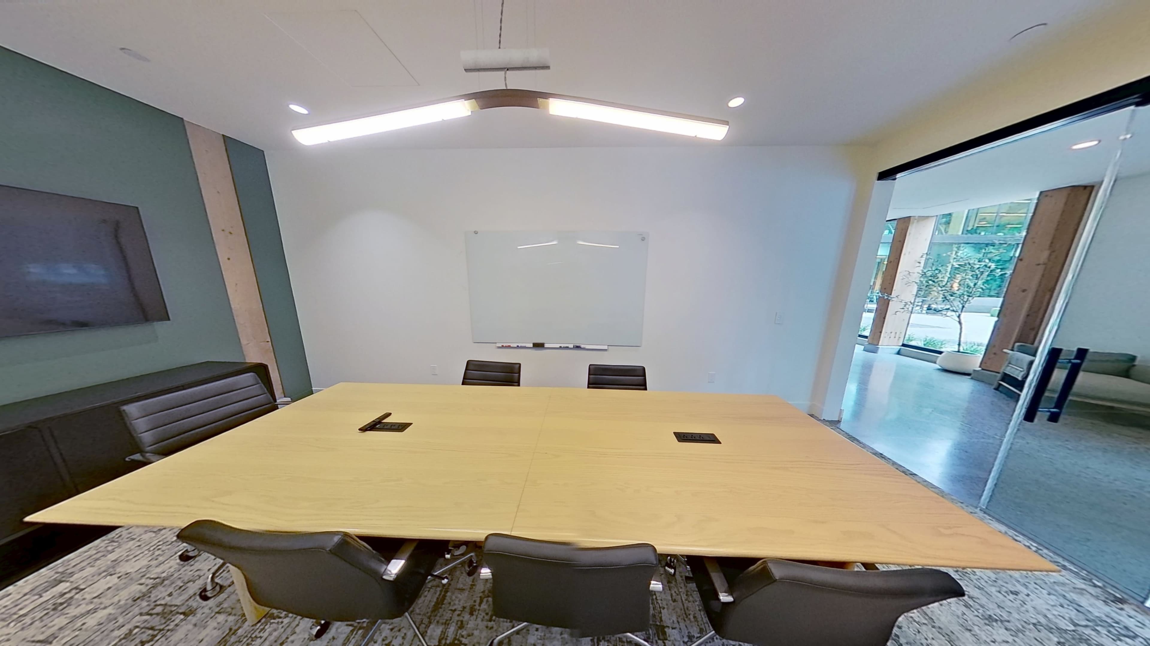 A large conference room features a wooden table surrounded by black chairs, with a whiteboard and wall-mounted screen in the background.