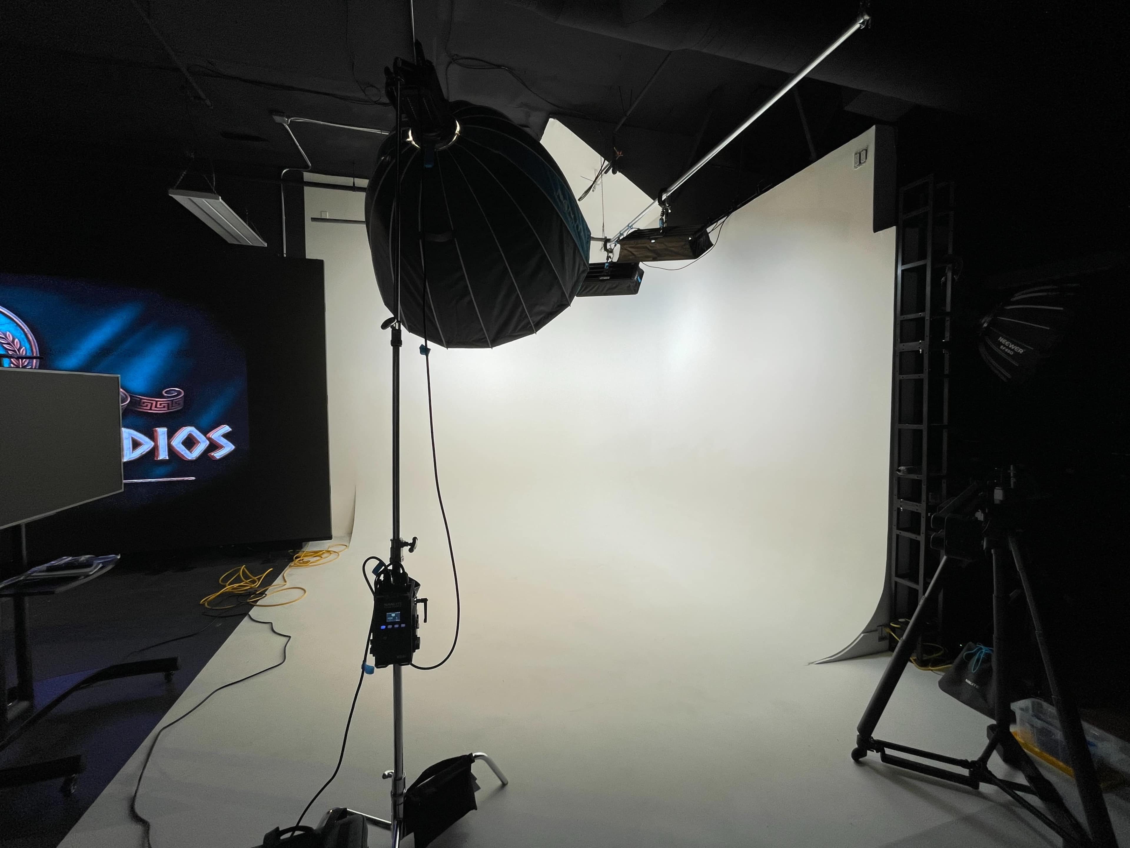 The image shows a photography studio with a white backdrop, lighting equipment, and a darkened area suggesting preparations for a photo or video shoot.