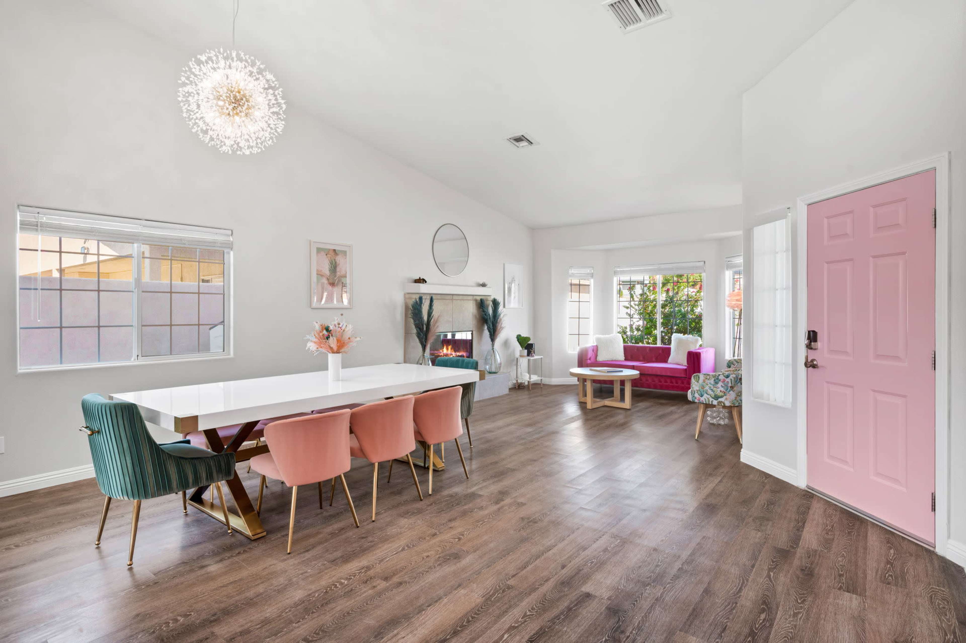 A spacious living area features a dining table with colorful chairs, a cozy seating area, and large windows allowing natural light.