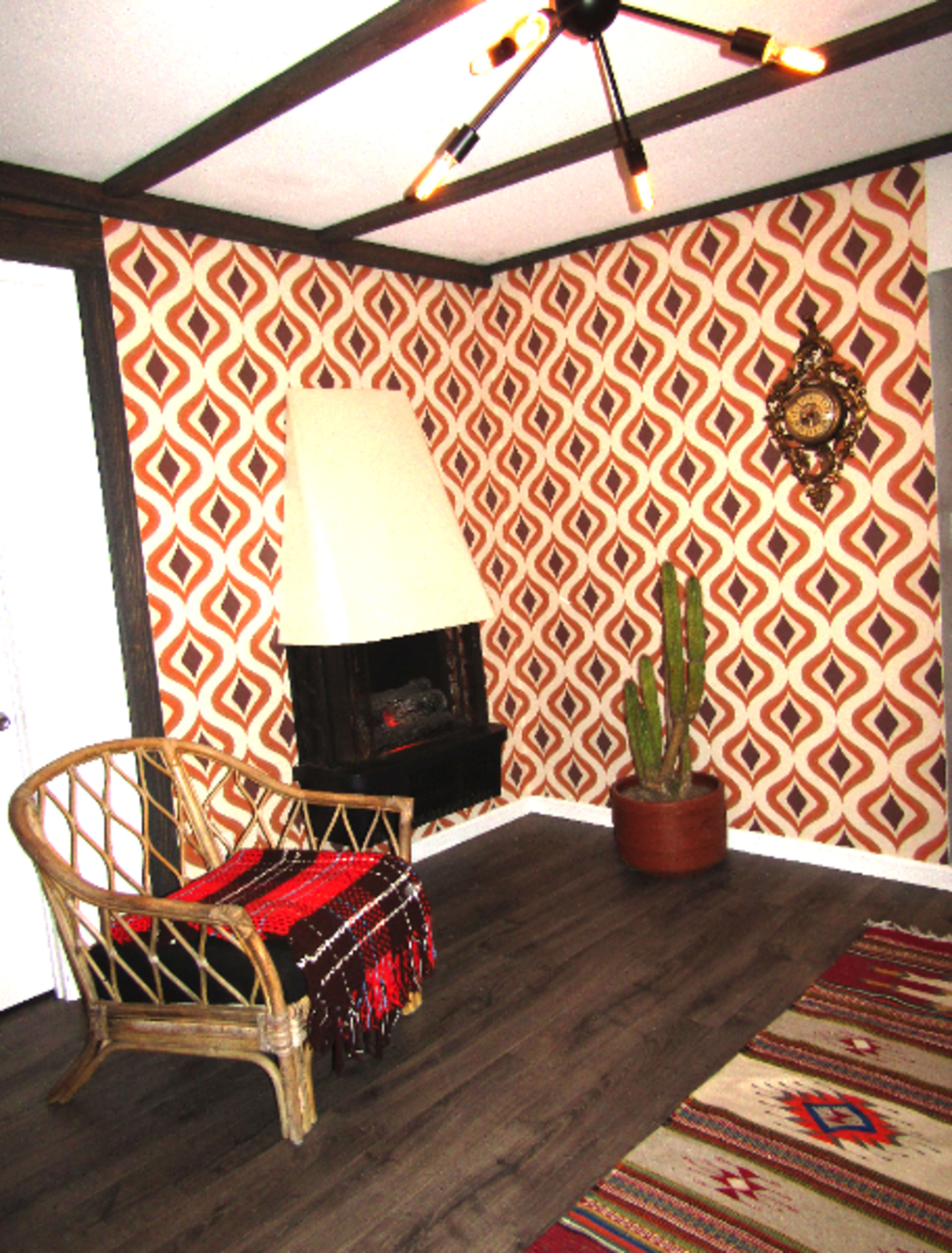 The image shows a room with geometric patterned wallpaper, a wicker chair with a blanket, a potted cactus, and a fireplace.