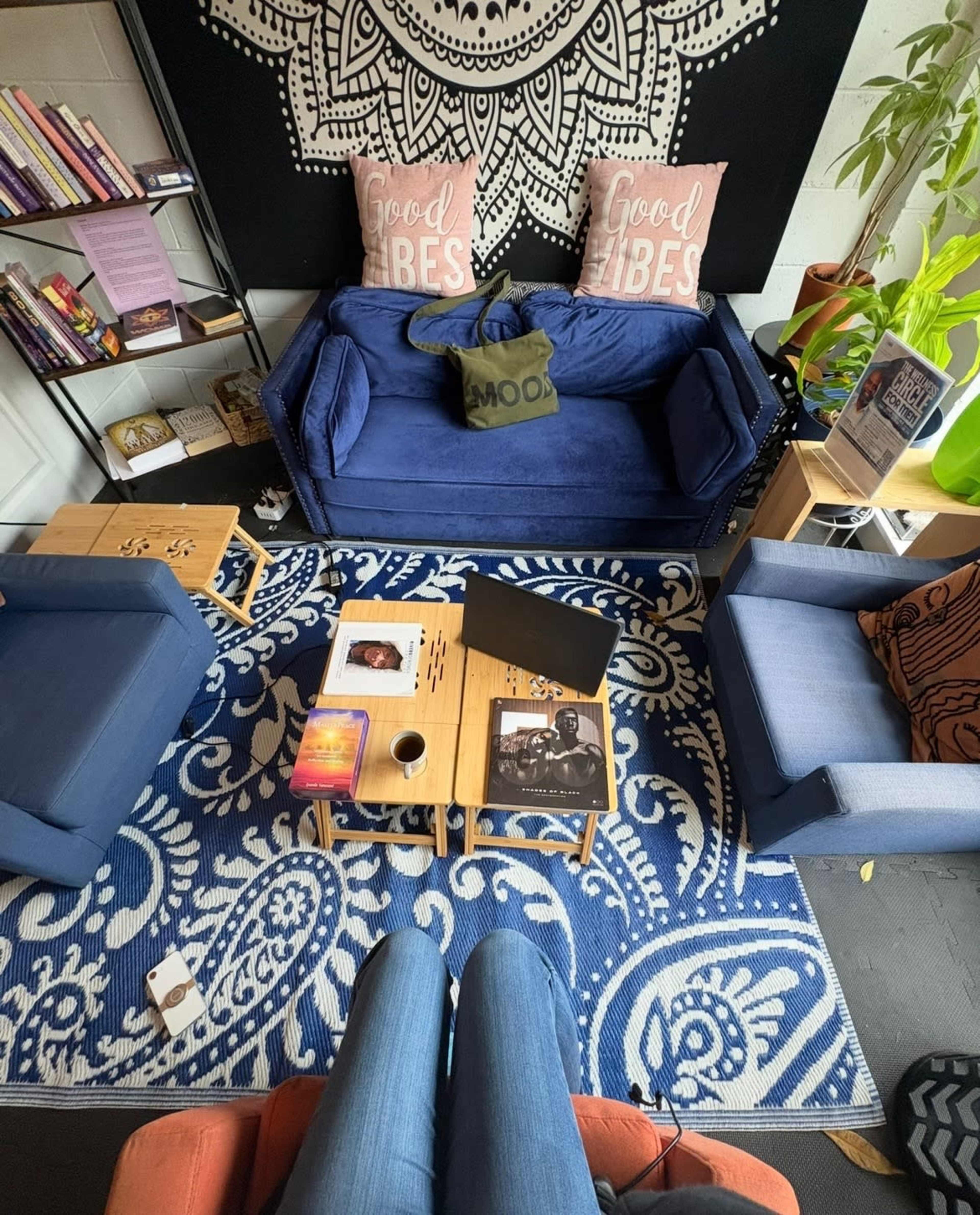The image shows a cozy seating area with a blue sofa, two blue chairs, wooden tables, and decorative pillows that read "Good Vibes," all arranged on a patterned rug.