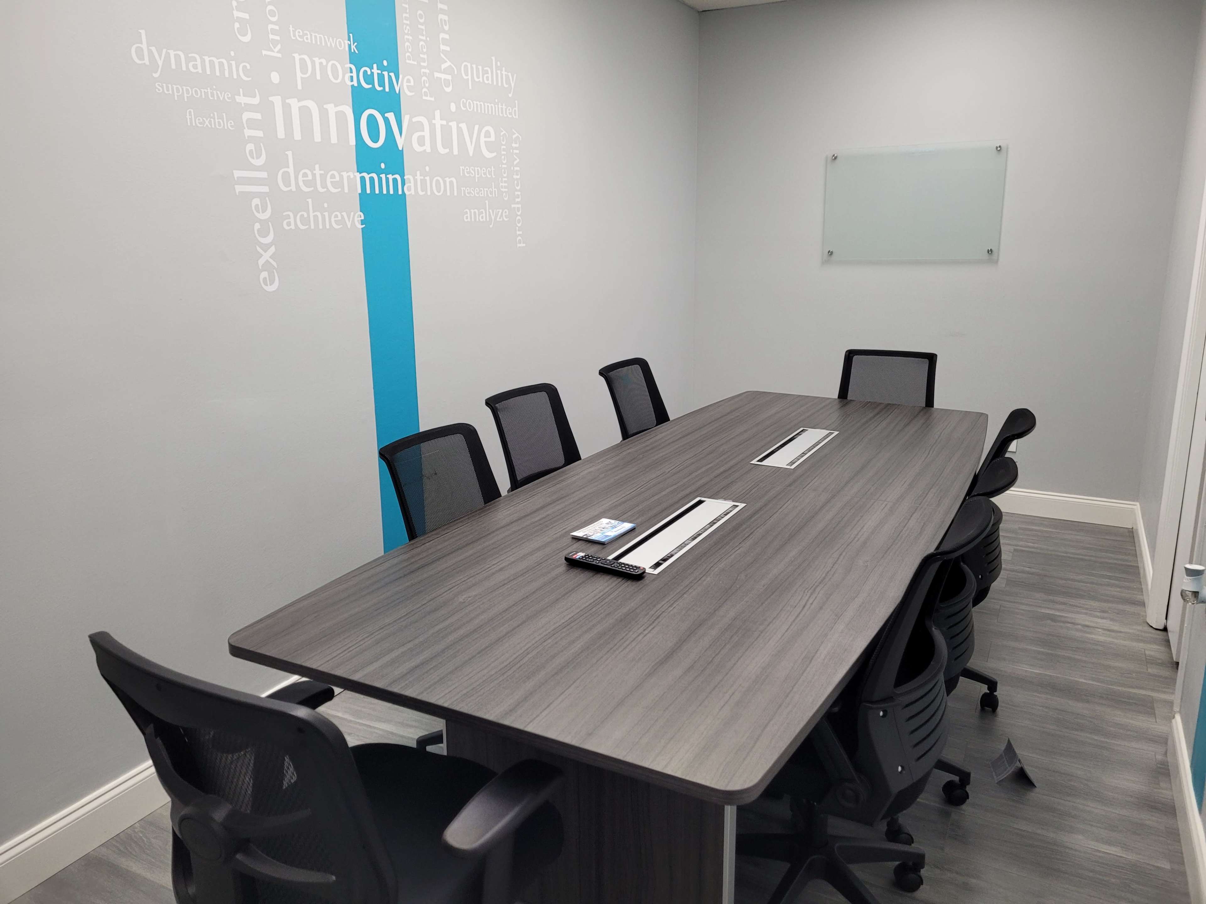 A modern conference room features a long table with multiple black chairs and wall text emphasizing business values.