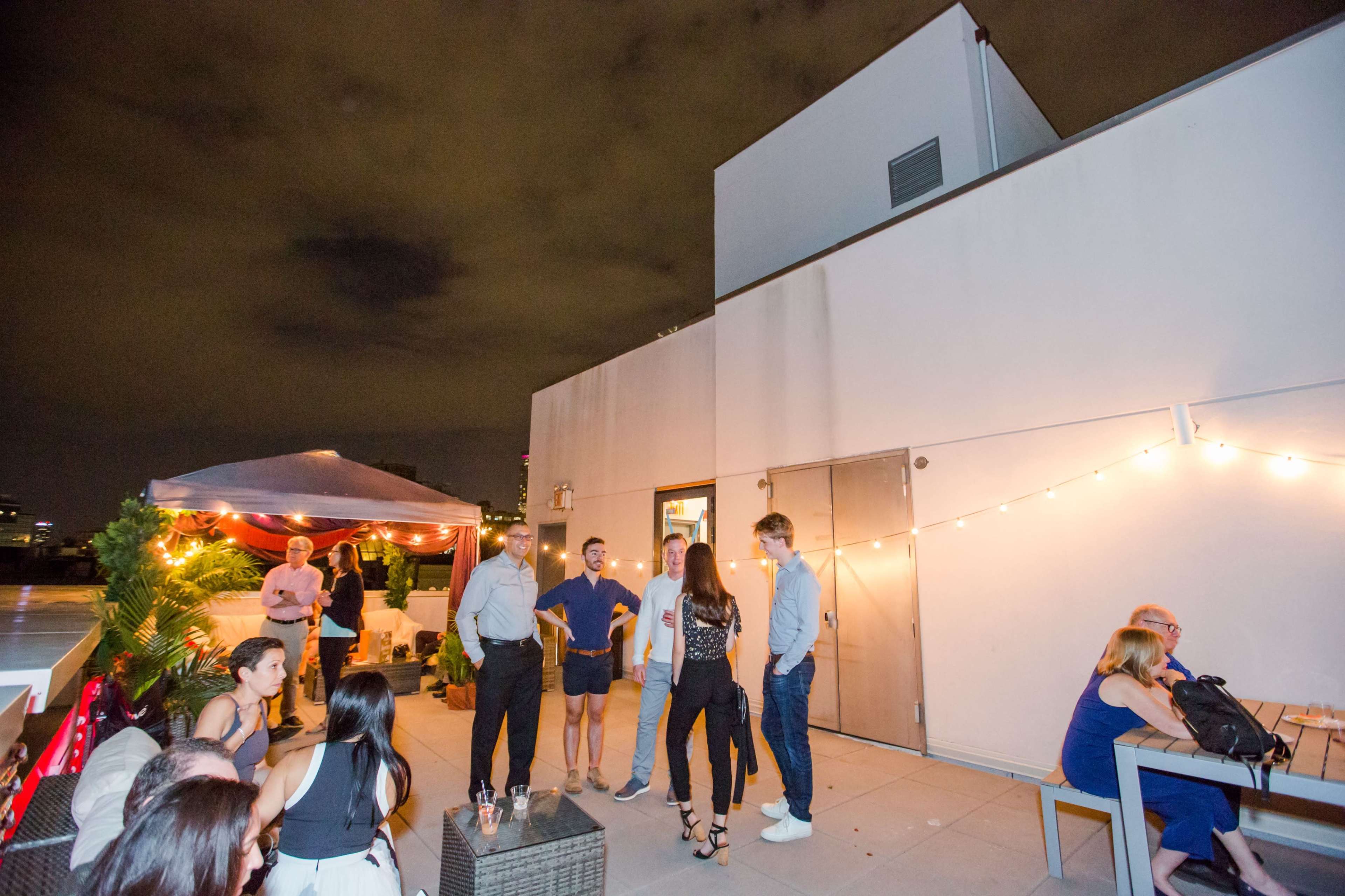 A group of people socializes on a rooftop terrace adorned with string lights and a tented area.