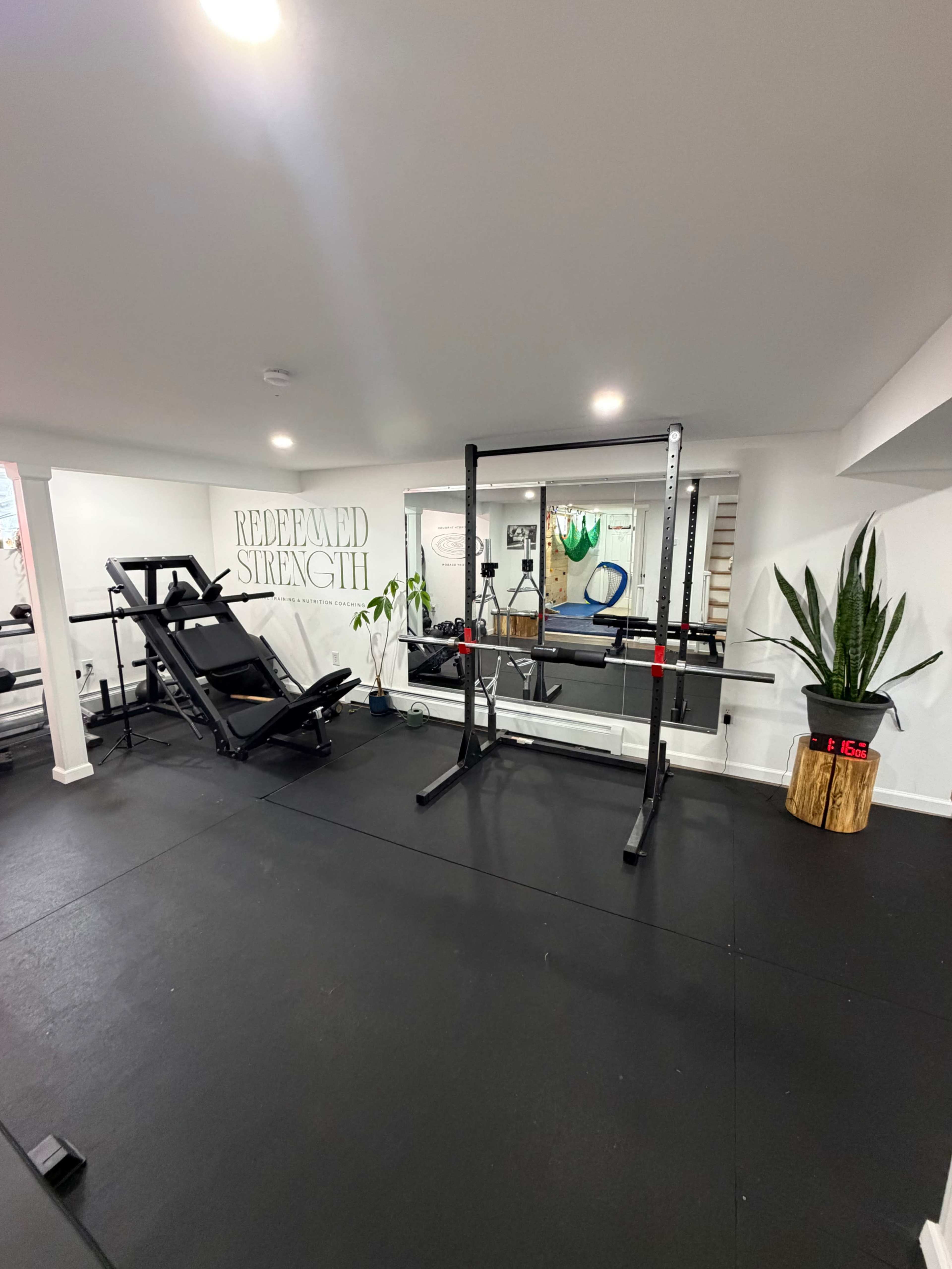 The image shows a well-equipped home gym featuring a weight bench, a squat rack, exercise equipment, and a motivational wall sign.