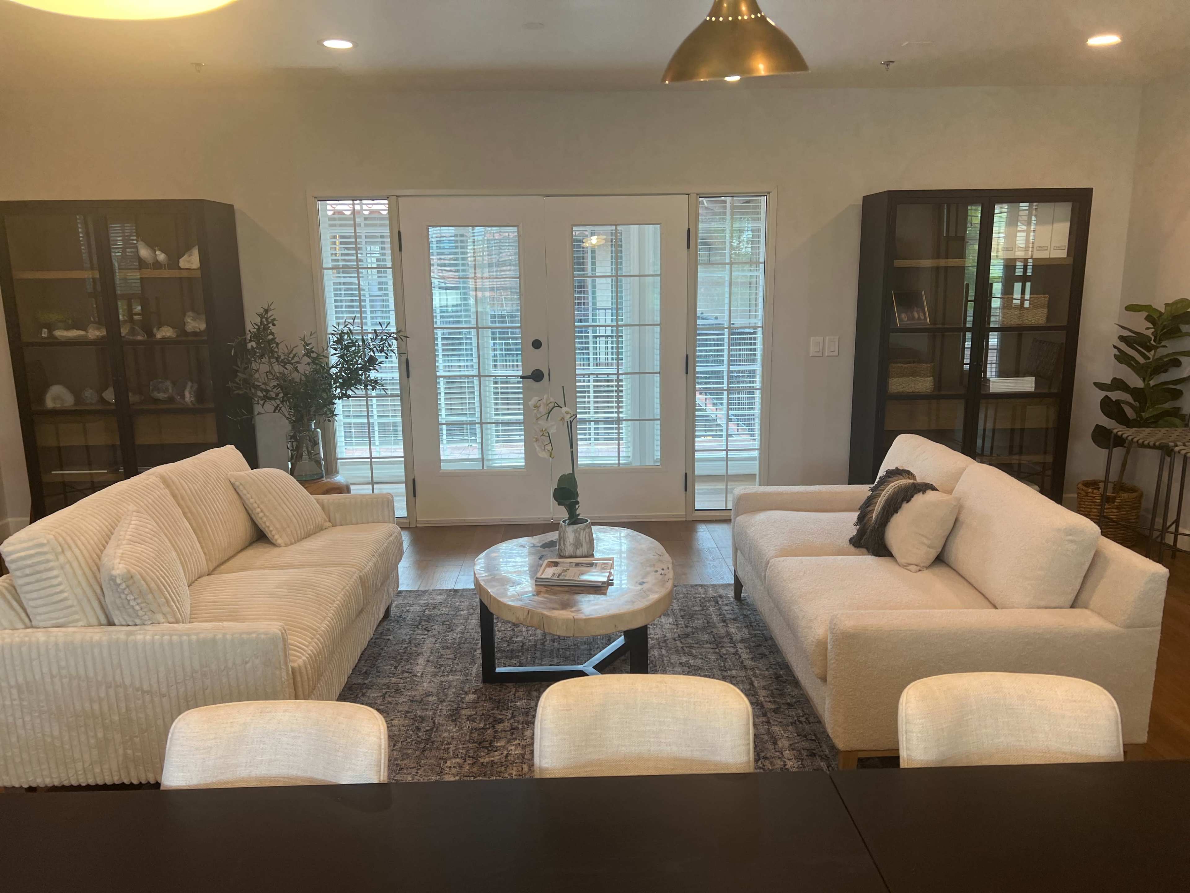 A living room with two sofas facing a round coffee table, surrounded by large windows and bookcases.