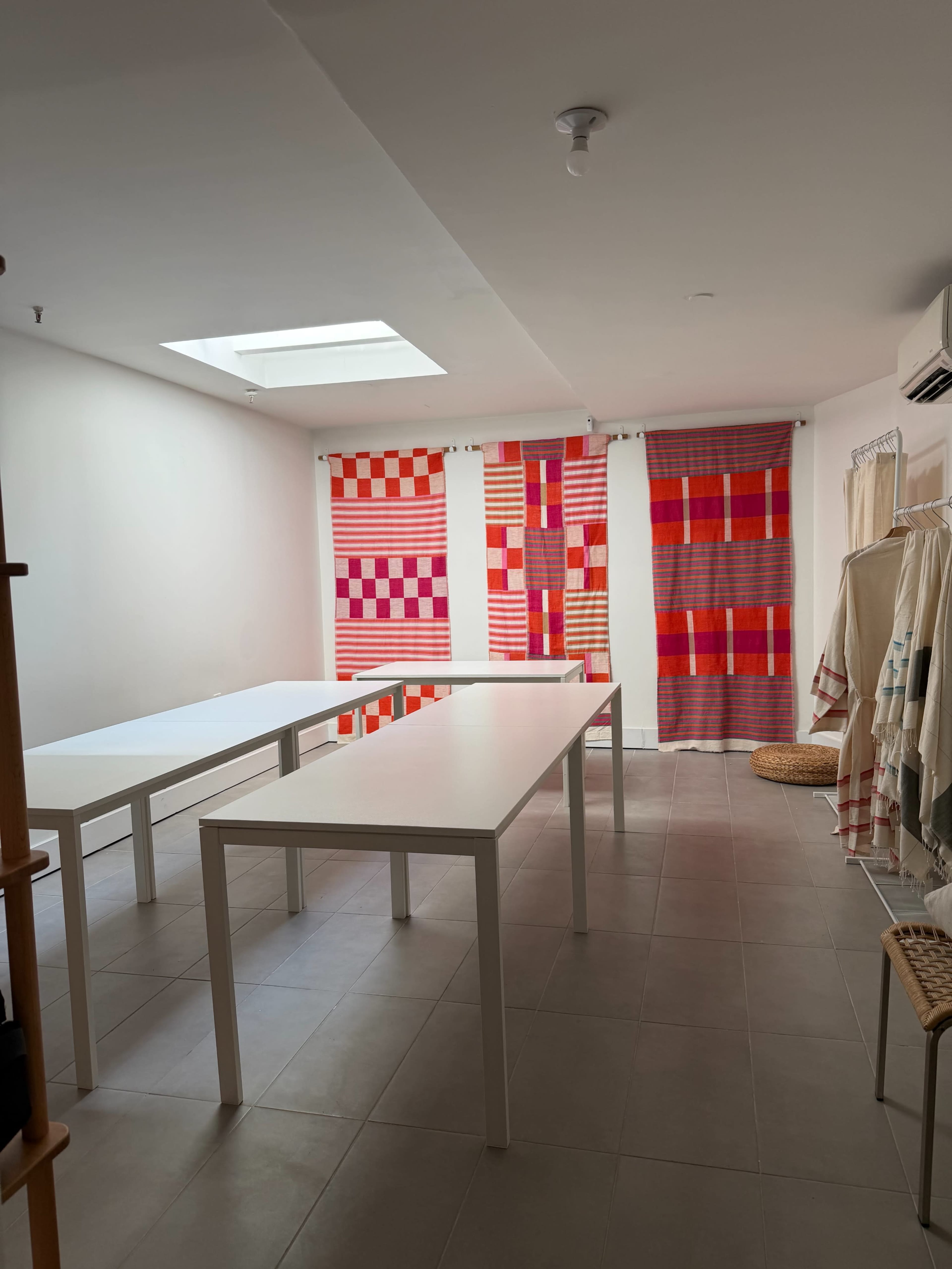 The image shows a well-lit room with white tables and colorful fabric panels hanging on the walls.
