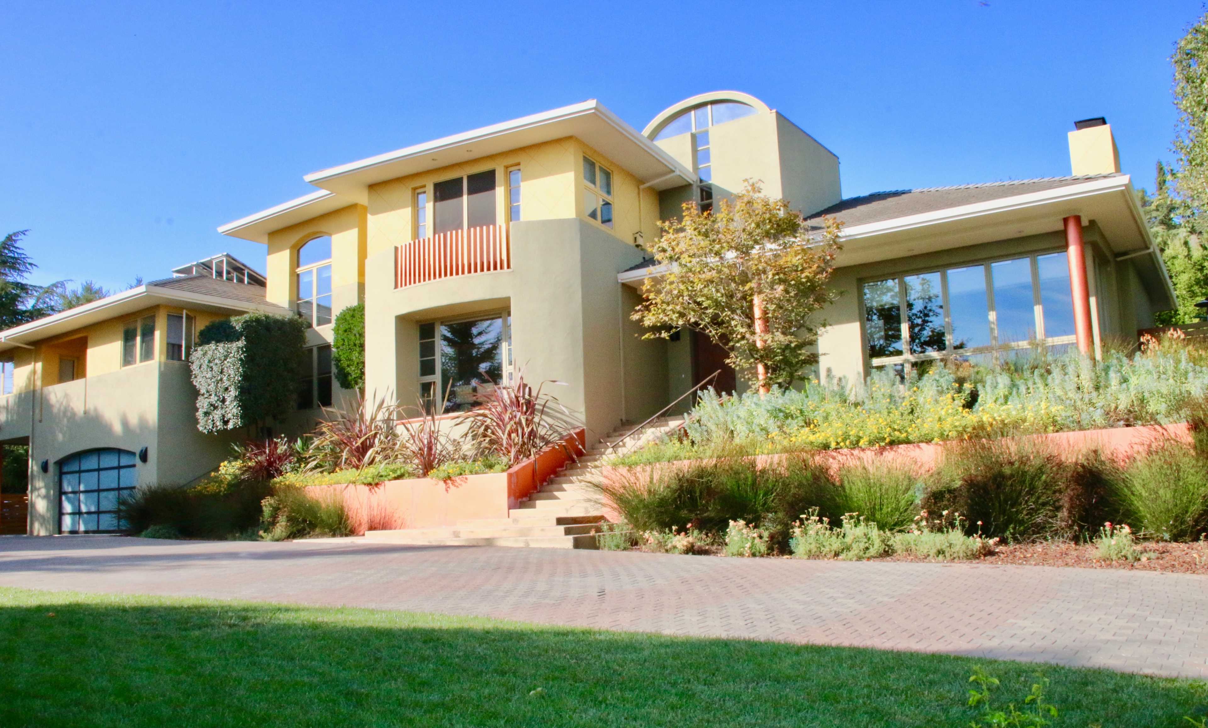 A modern two-story house with a landscaped front yard, flower beds, and a large driveway.