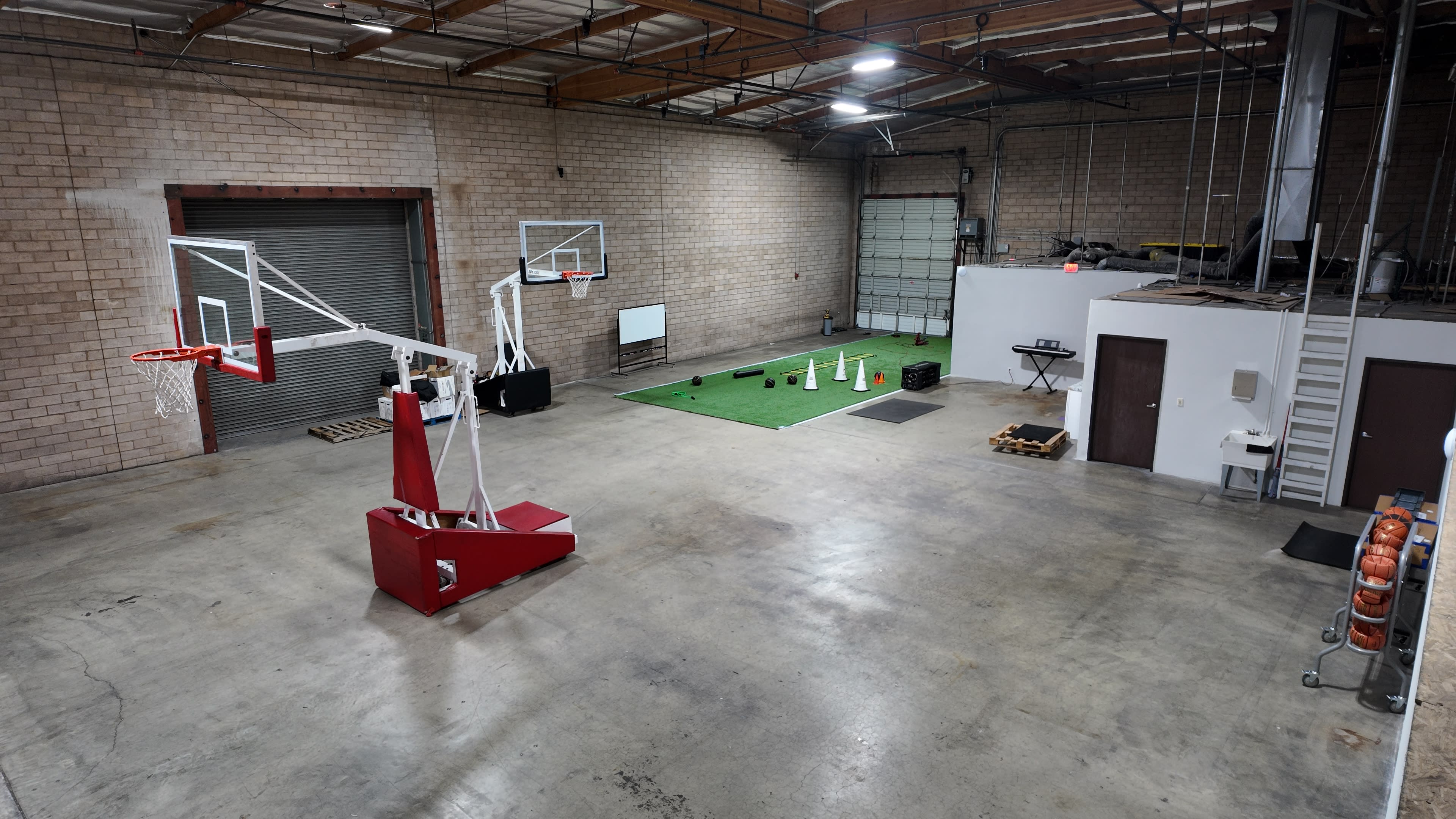 The image shows a spacious indoor facility with a basketball hoop on one side and turf area with various training equipment on the other.