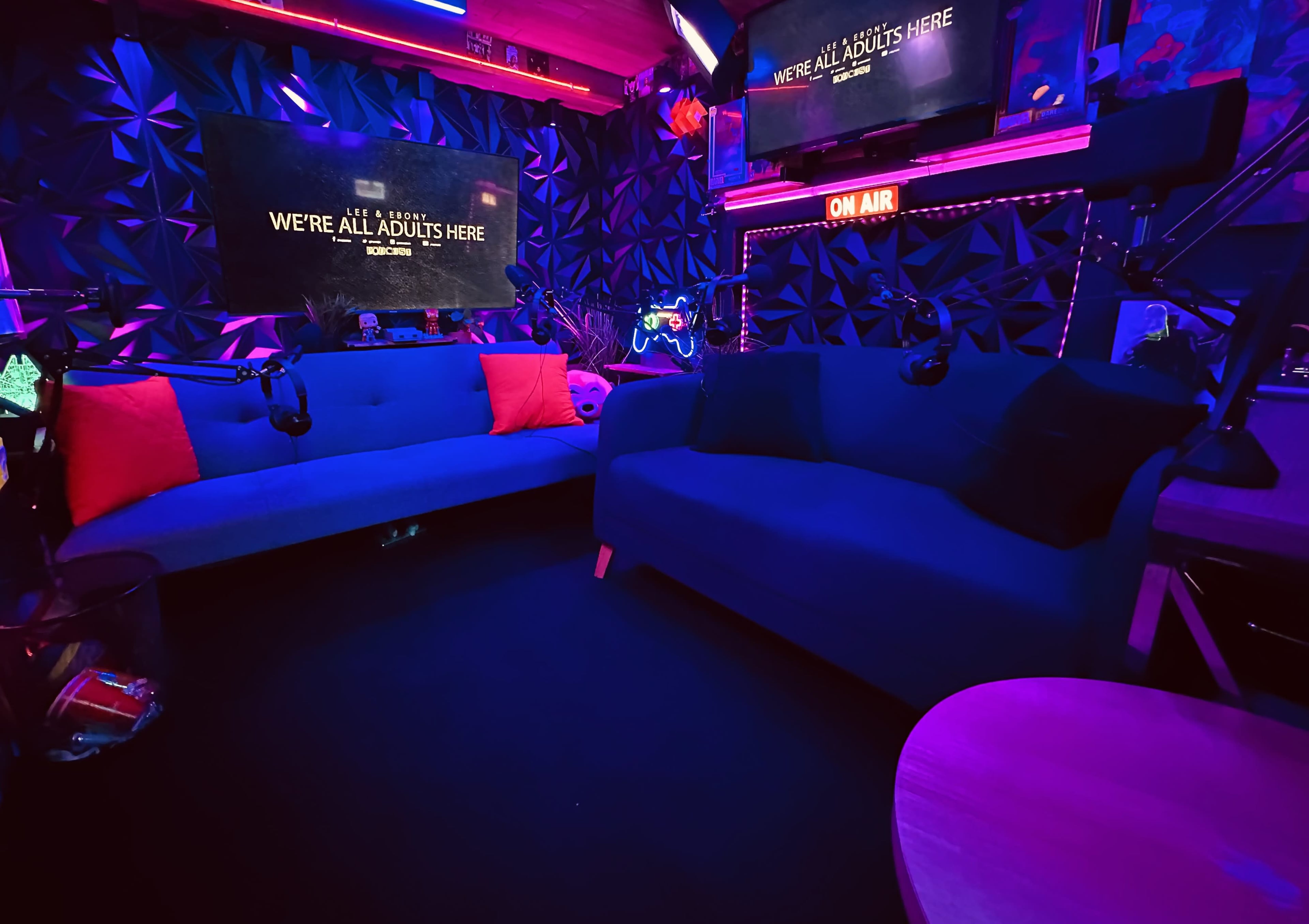 The image depicts a brightly lit studio with two blue sofas, decorative neon lighting, and screens displaying text against a textured wall.