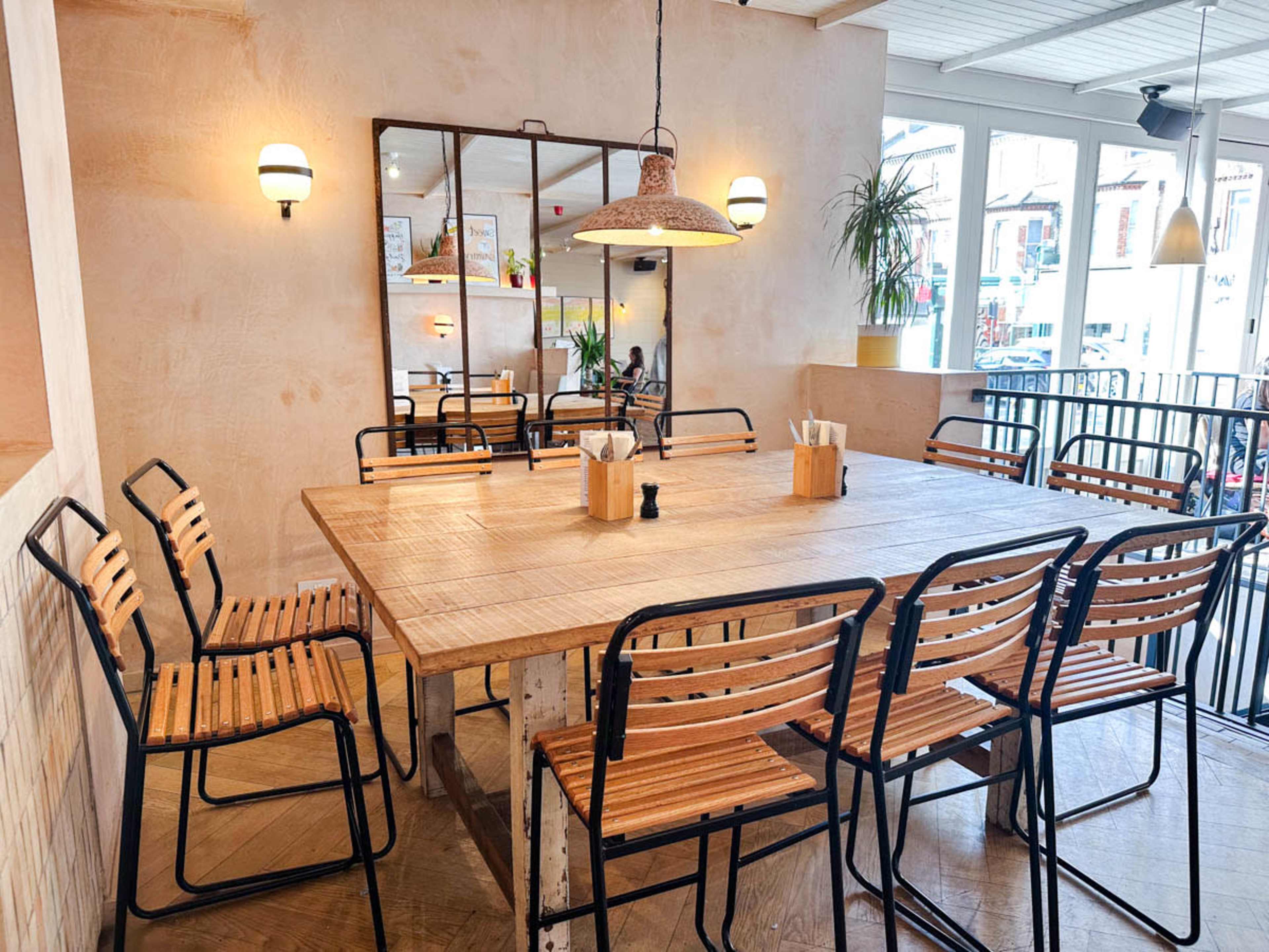 A spacious dining area with a large wooden table surrounded by metal-framed chairs and a mirrored wall reflecting the interior.
