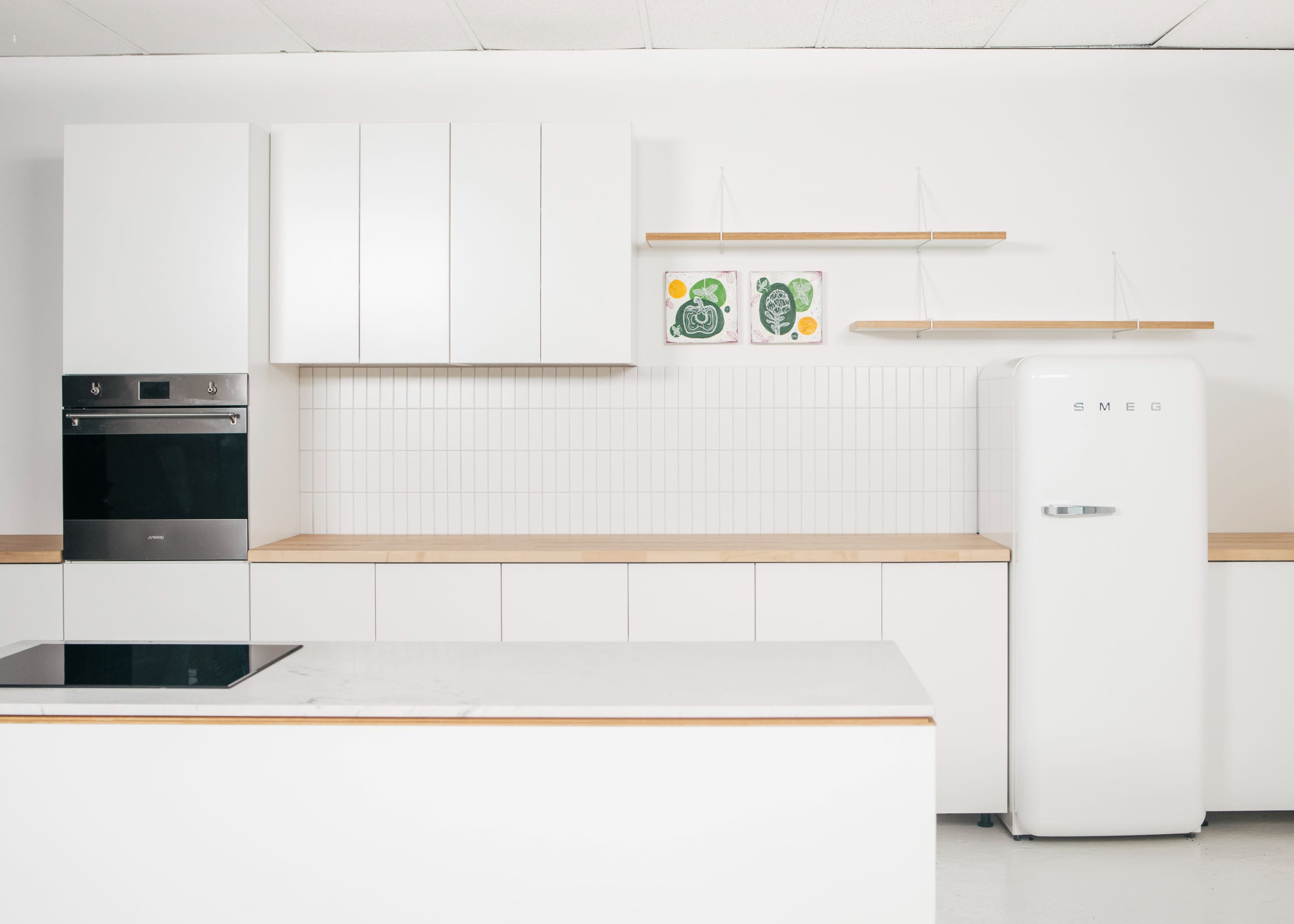 A modern kitchen featuring white cabinetry, a built-in oven, a minimalist open shelf, and a vintage-style white refrigerator.
