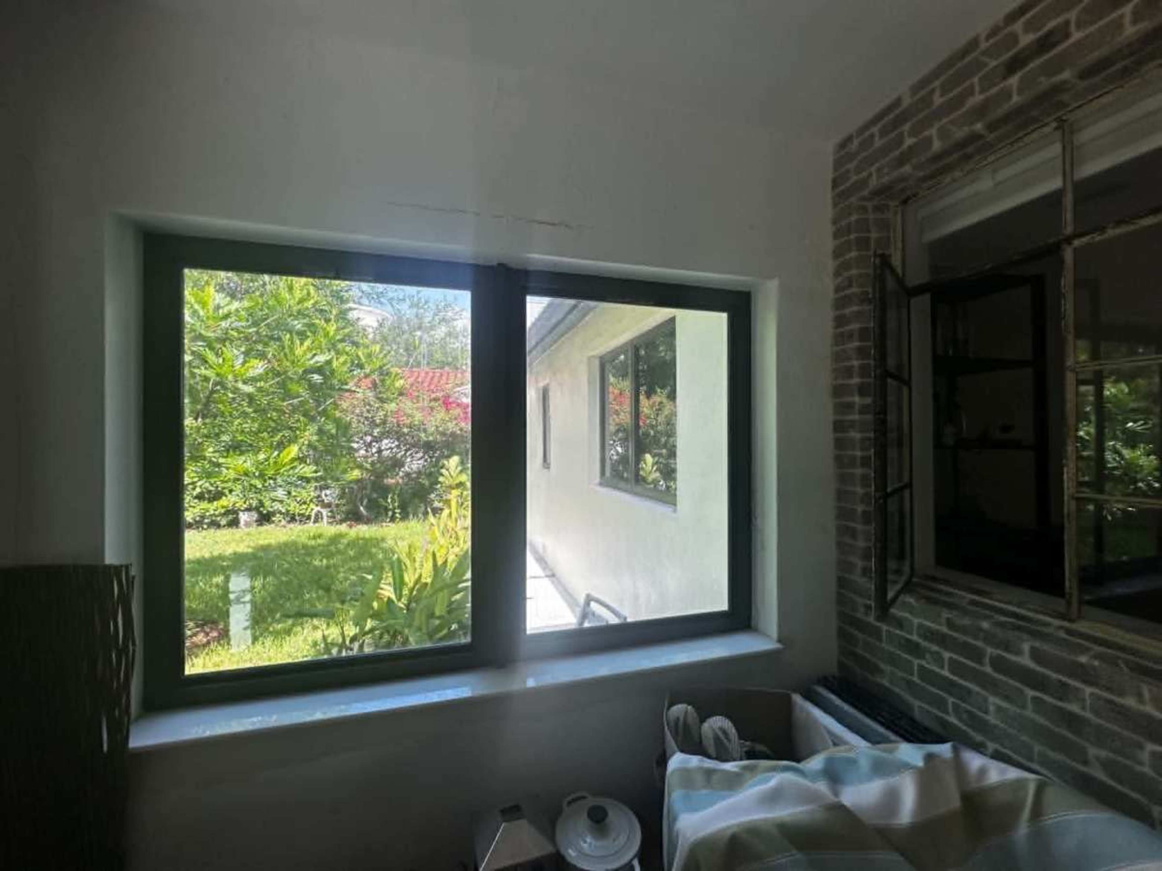 The image shows a view through a window, revealing a garden with greenery and a house exterior on the opposite side.
