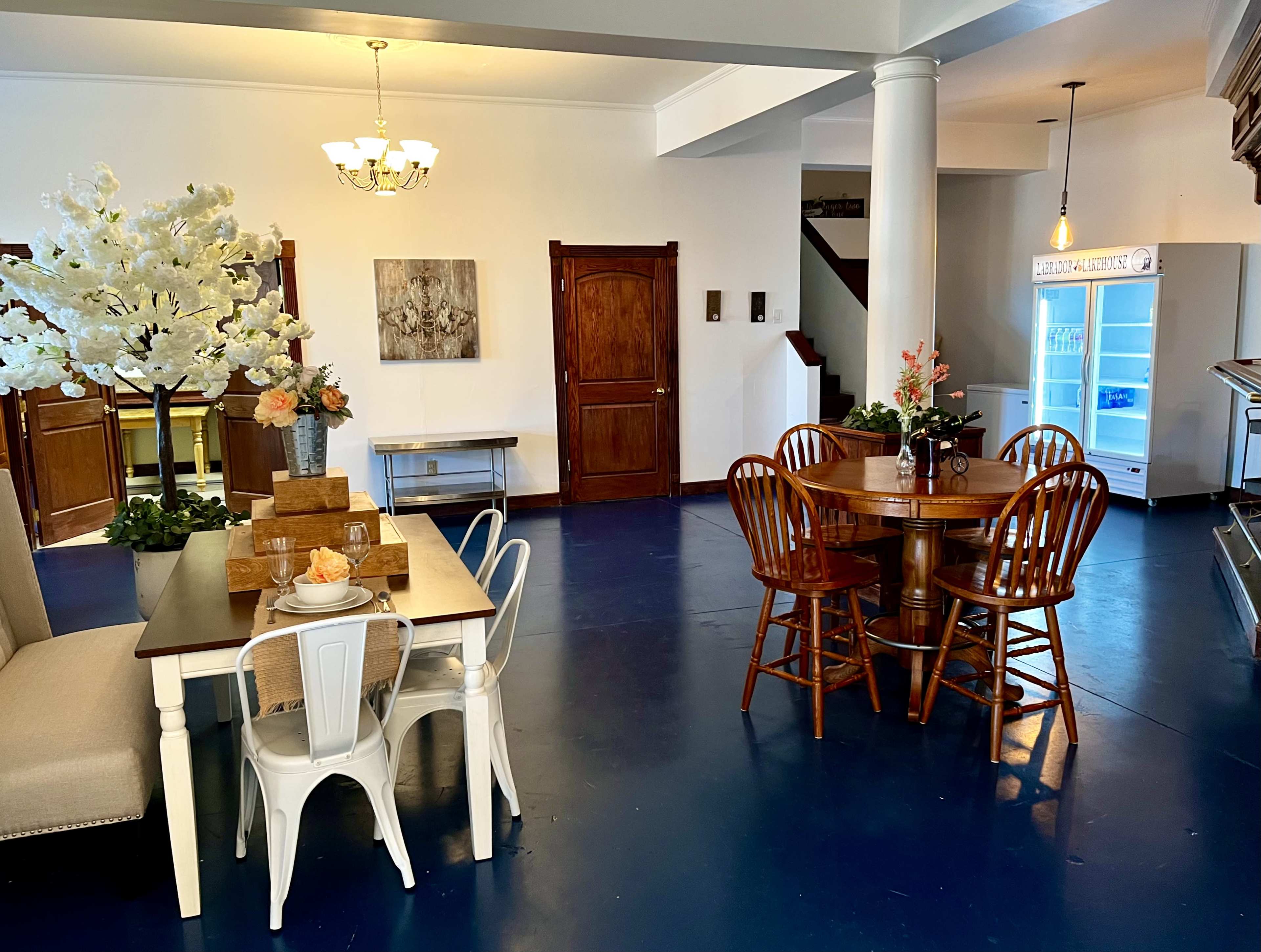 The image shows a spacious dining area featuring two tables, a decorative white tree, and a refrigerator in the corner.