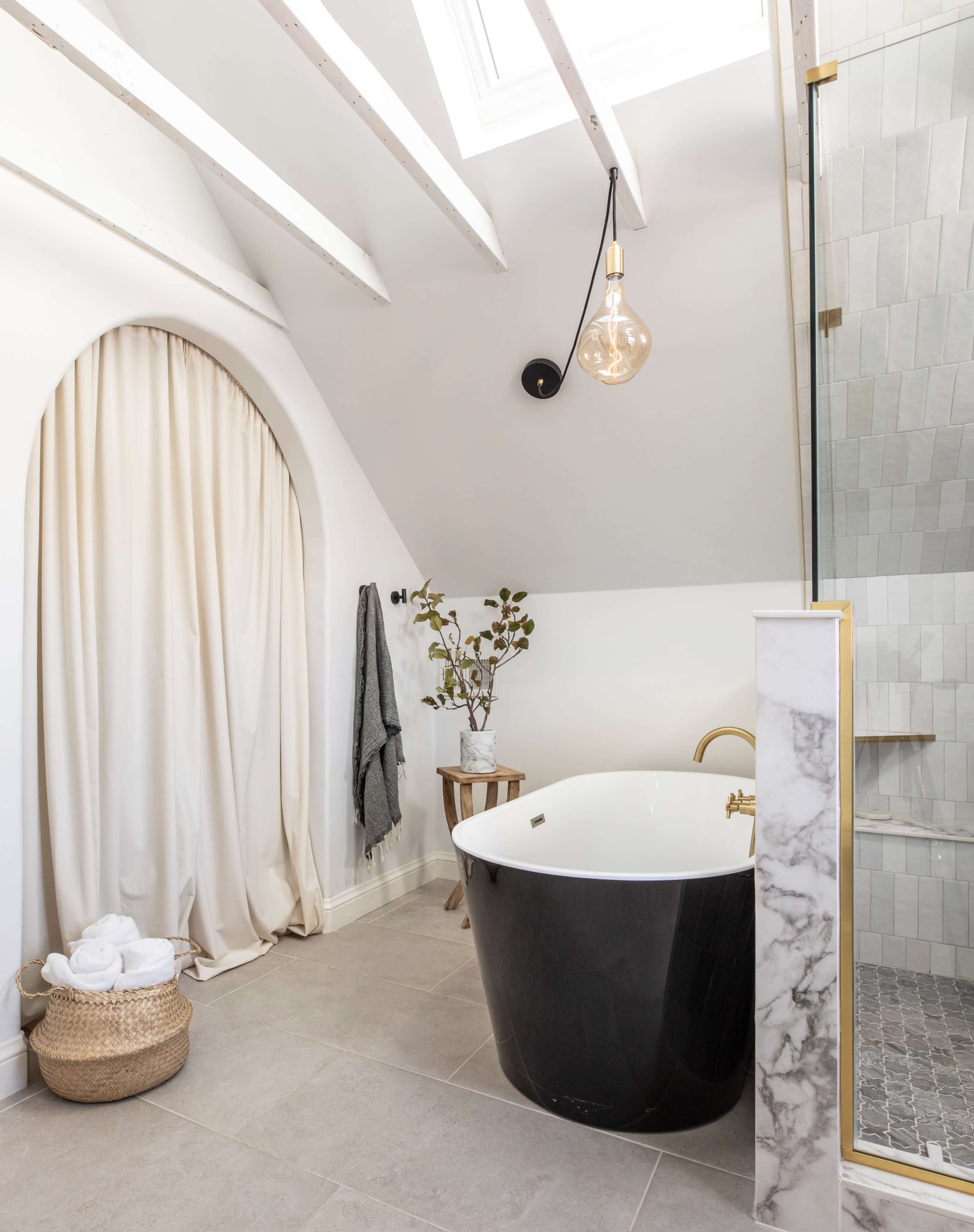The image features a modern bathroom with a freestanding black bathtub, a glass shower enclosure, and a decorative curtain alongside a potted plant on a wooden stool.