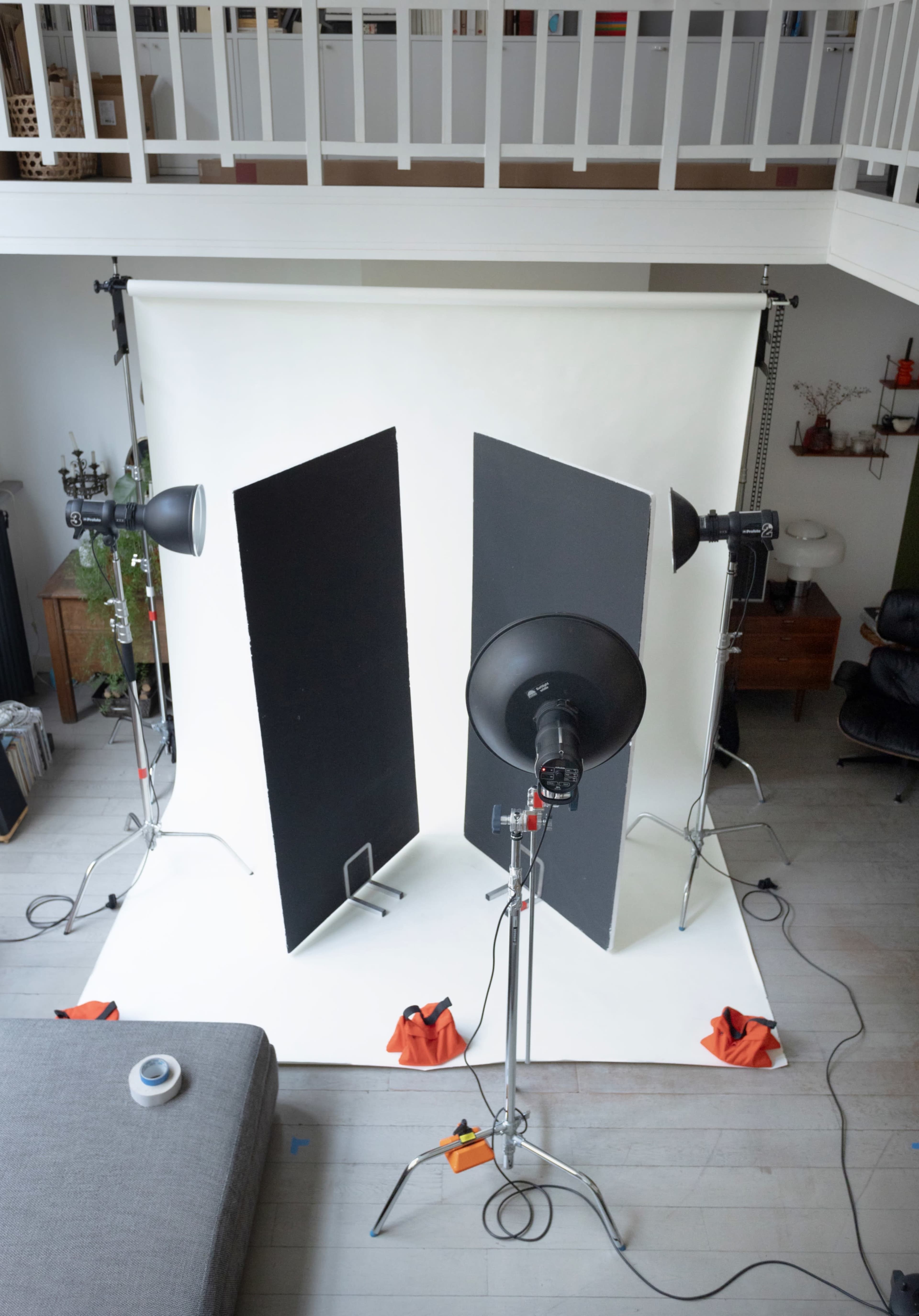 A photography studio setup features two backdrop panels, lights on stands, and a white floor, all arranged within a spacious room.