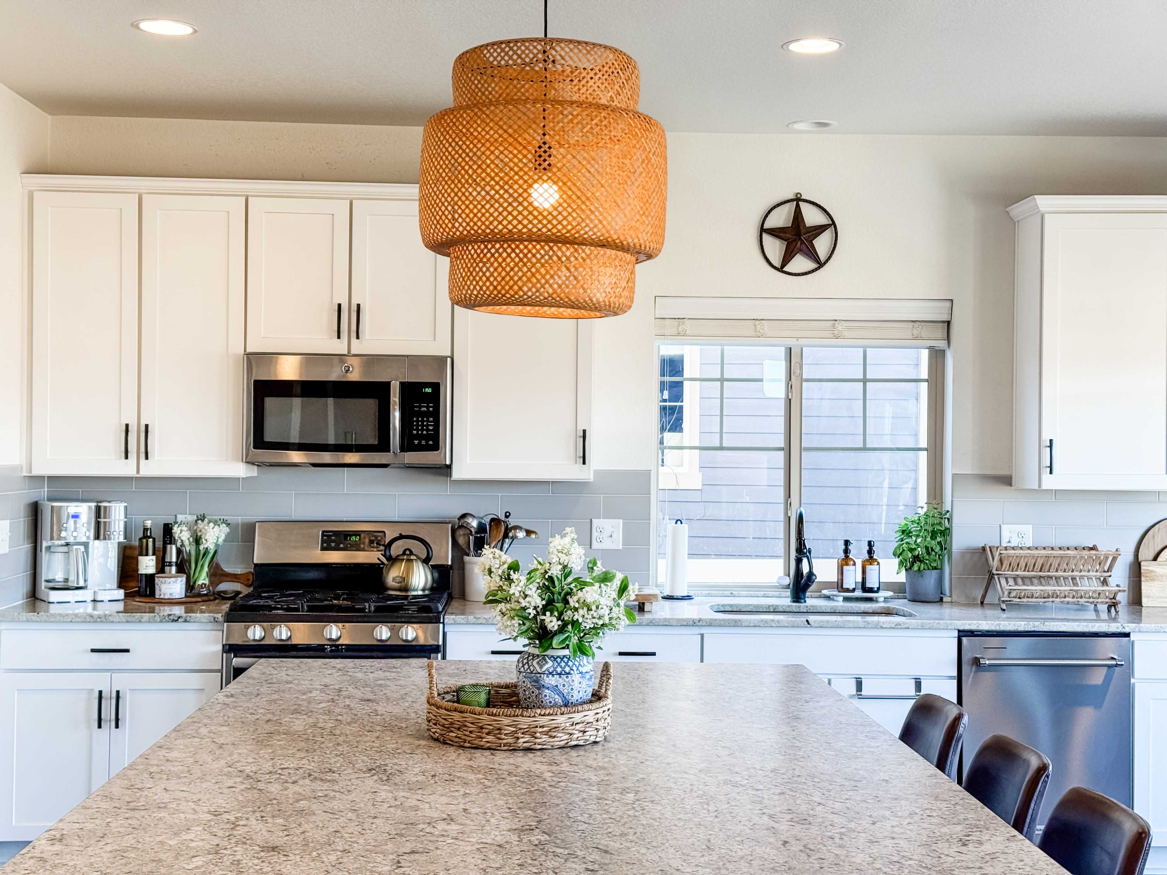 A modern kitchen features white cabinetry, a central island with a woven basket, and a large pendant light hanging above.