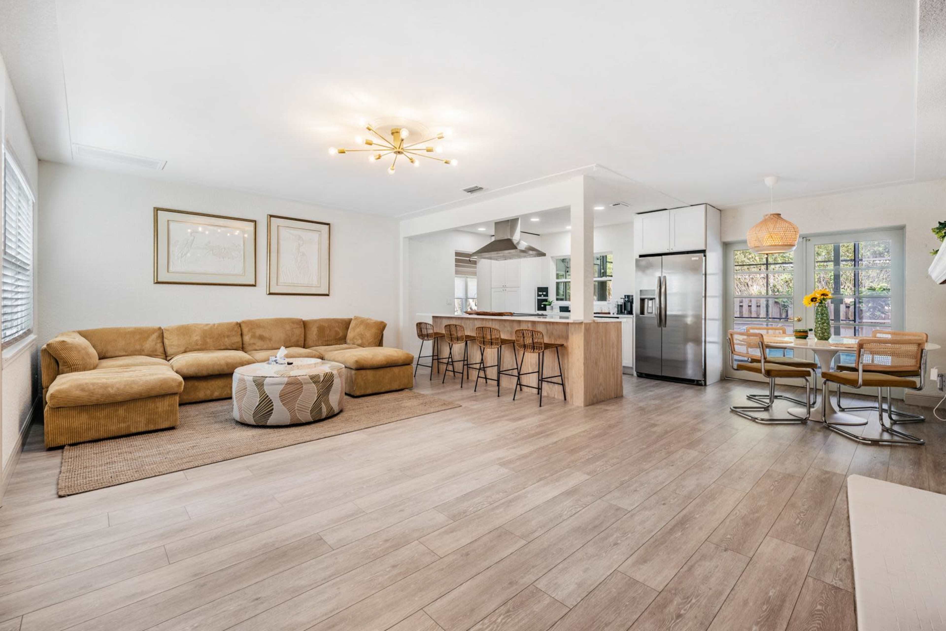 A modern, open-concept living space with a beige sectional sofa, a circular coffee table, a kitchen island with bar stools, and a dining area with a round table.