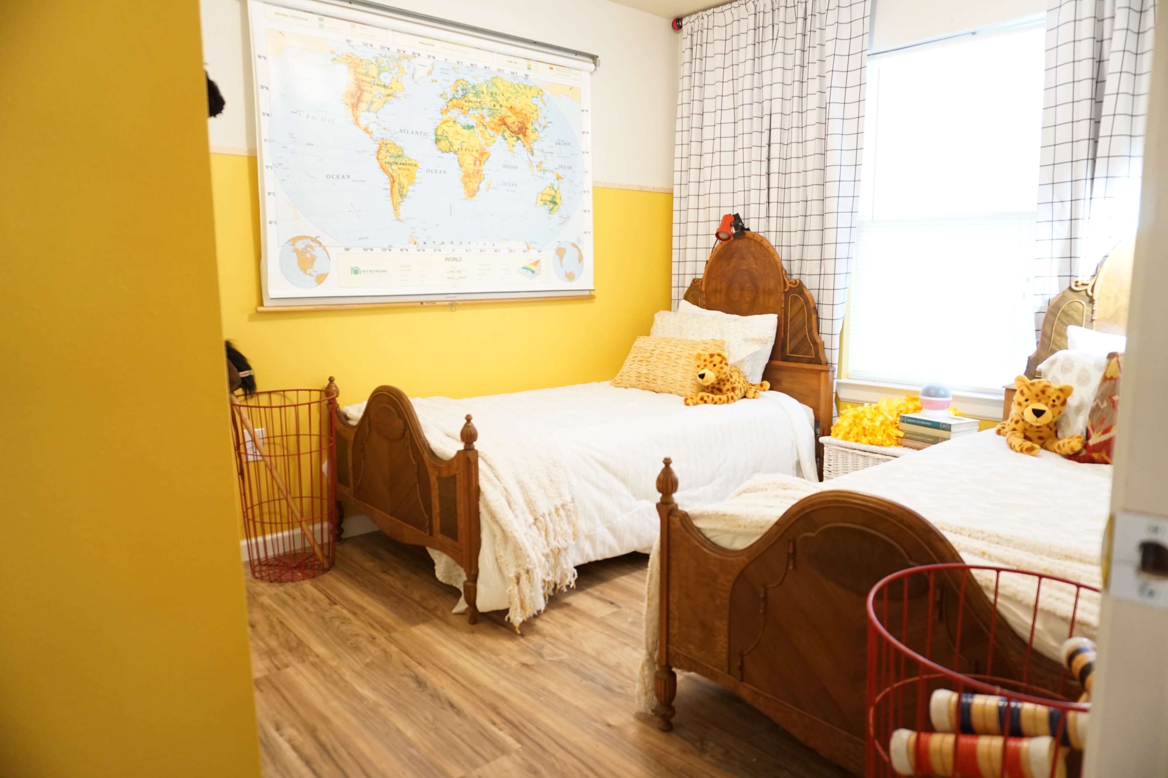 A bright yellow room with two beds, a world map on the wall, and stuffed animals on the pillows.