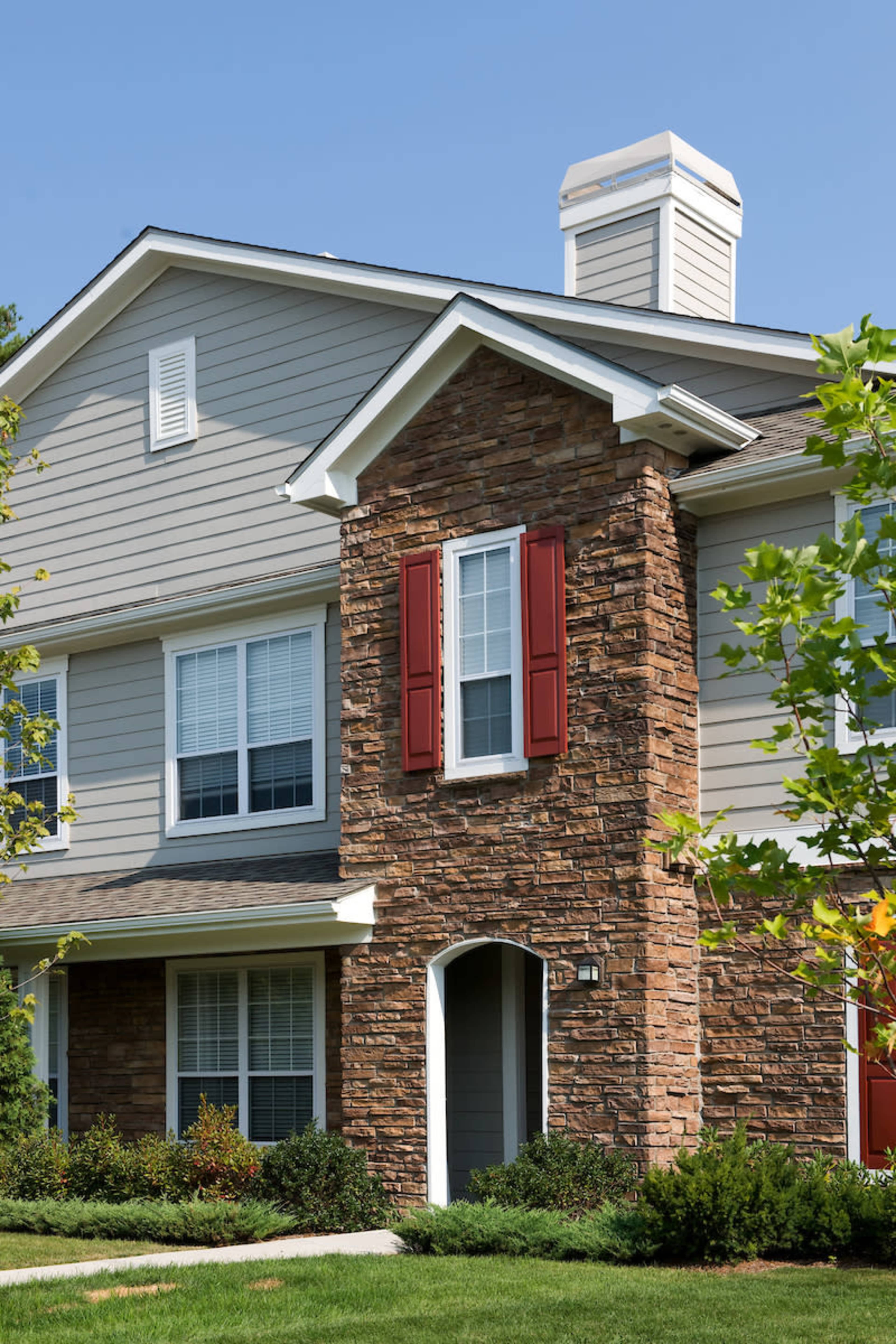The image shows a two-story house featuring a stone facade, red shutters, and a landscaped front yard.