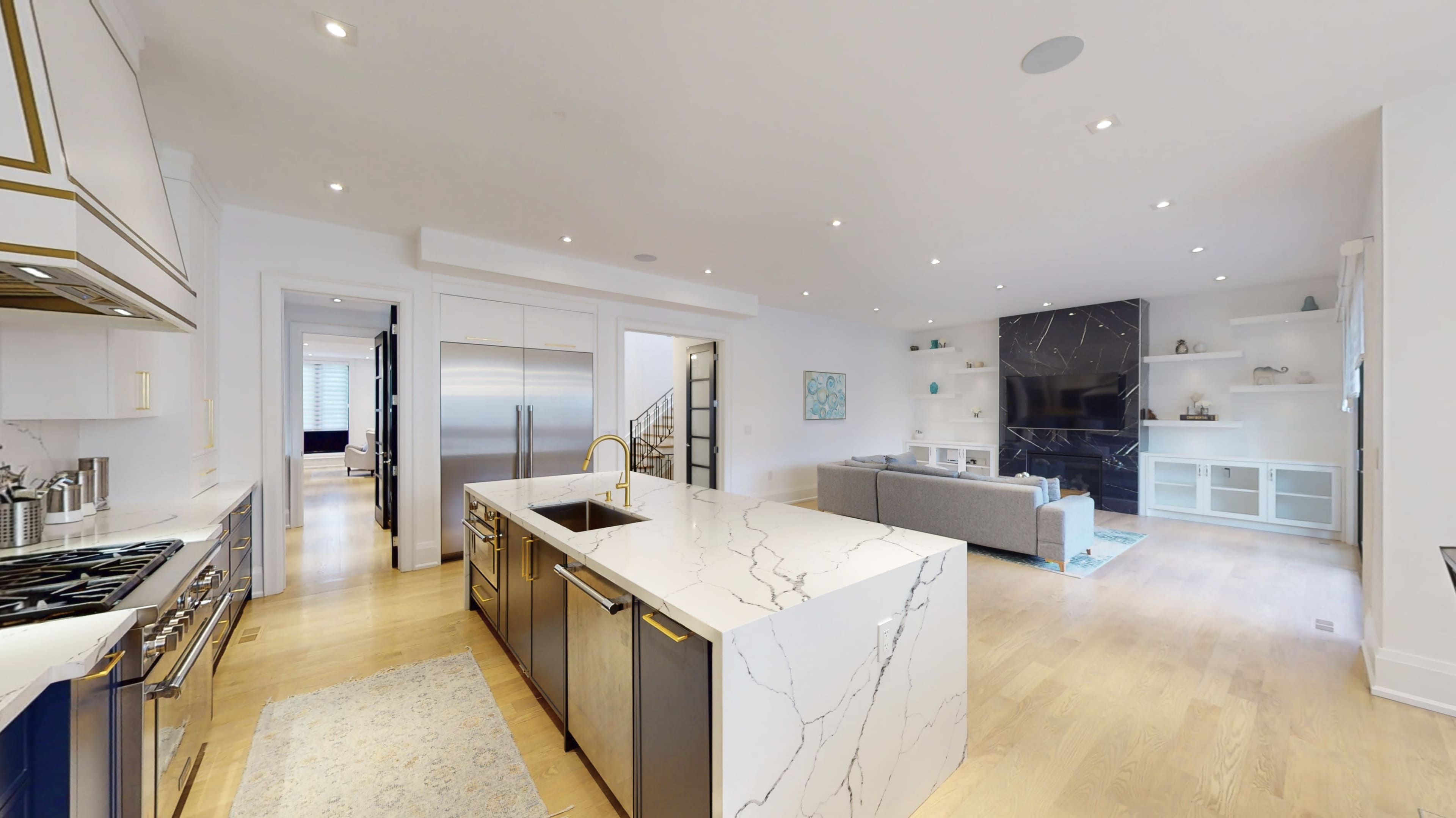 A modern kitchen with a central island, stainless steel appliances, and a connected living area featuring a couch and a large flat-screen TV.