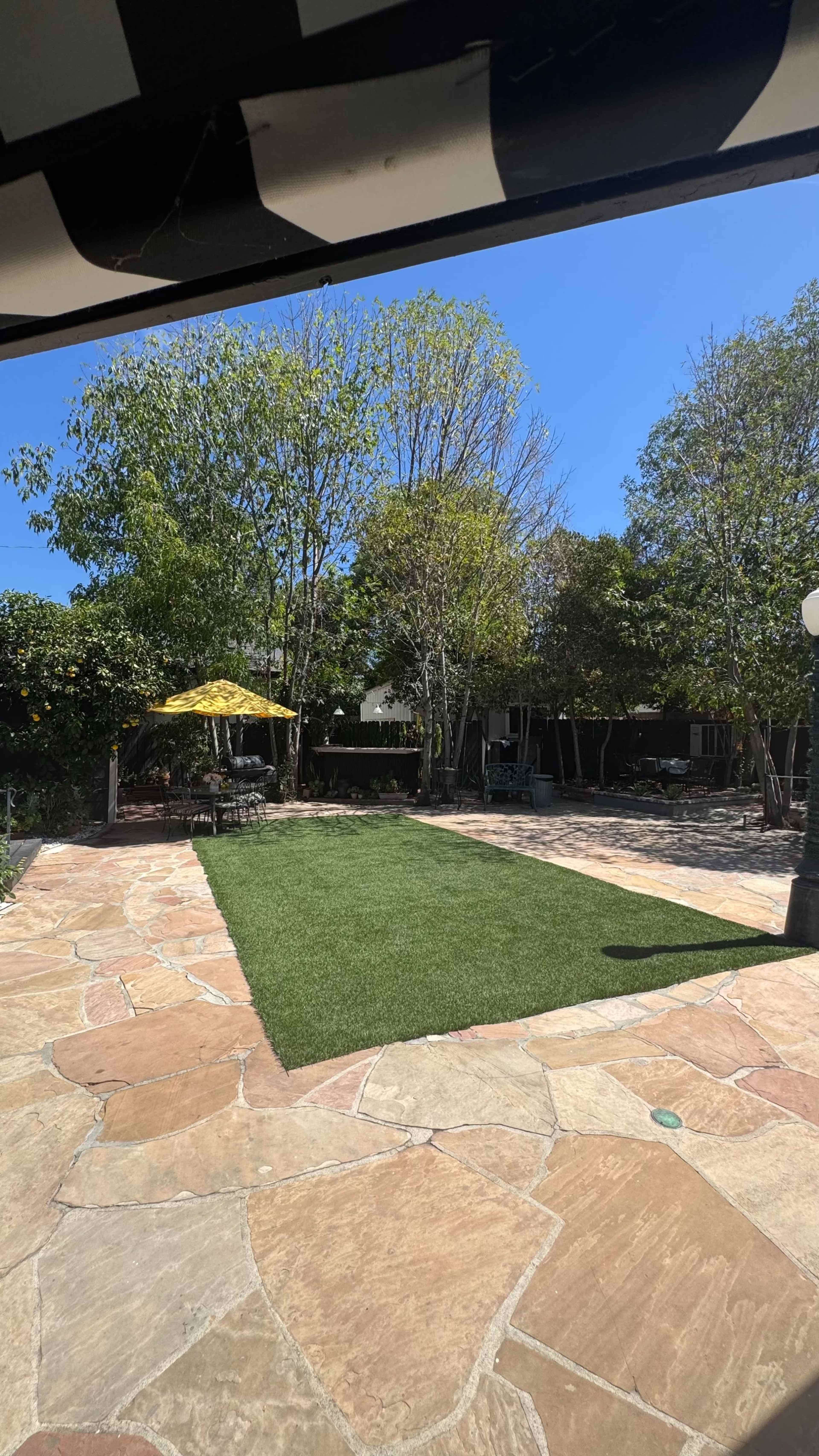 A spacious outdoor patio features a green lawn area, surrounded by trees and a yellow patio umbrella.
