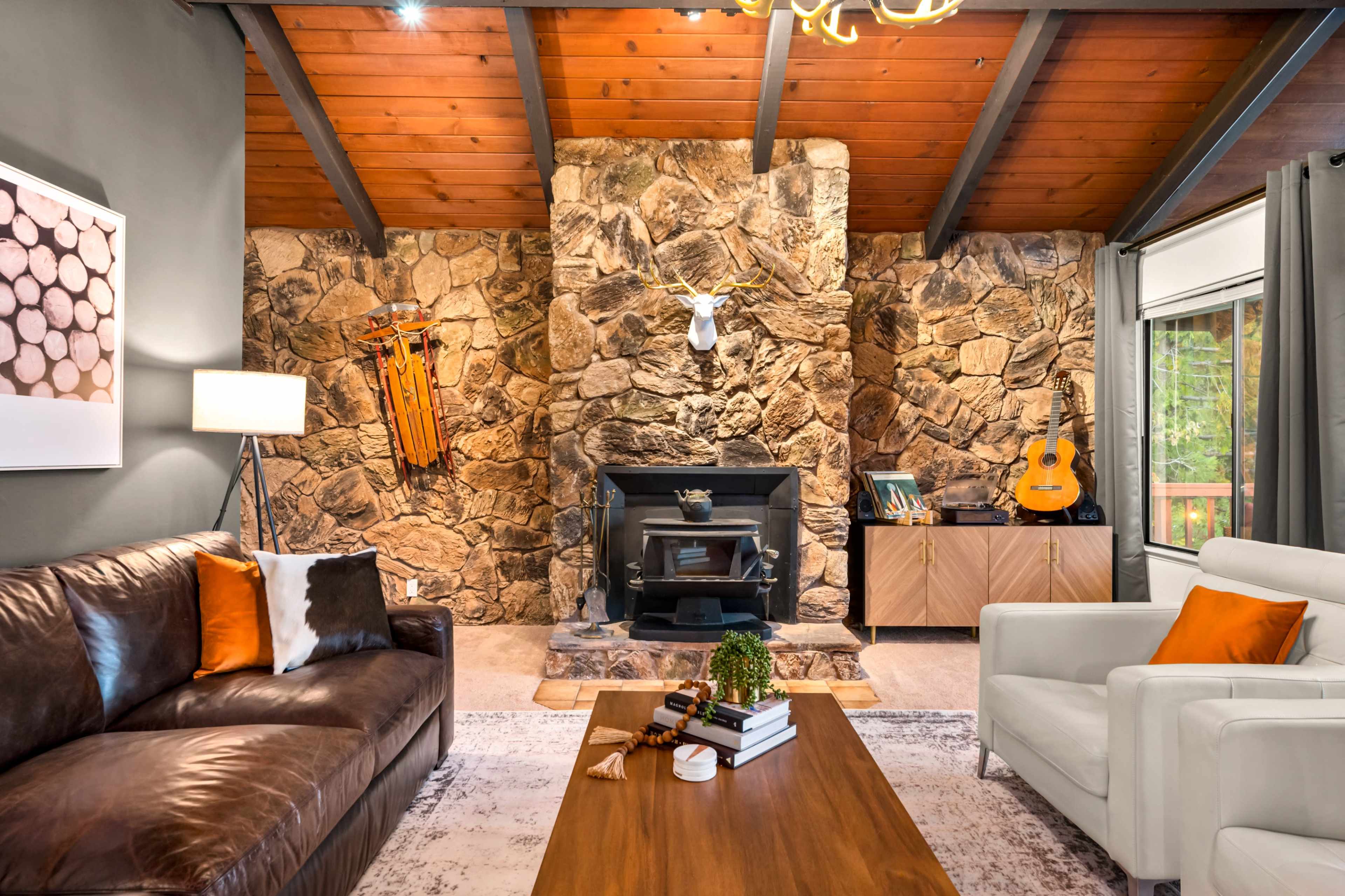 A cozy living room featuring a stone fireplace, wooden beams, two couches, and a coffee table.