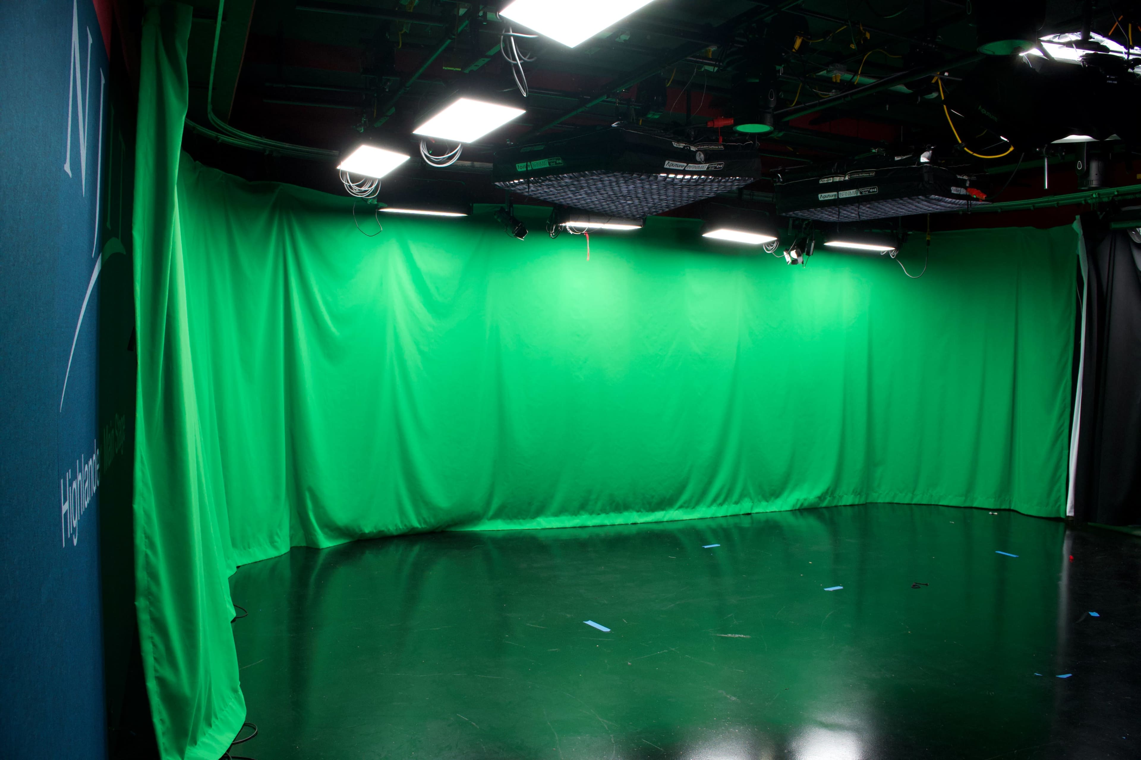 The image shows a studio space with a green screen backdrop and overhead lights.