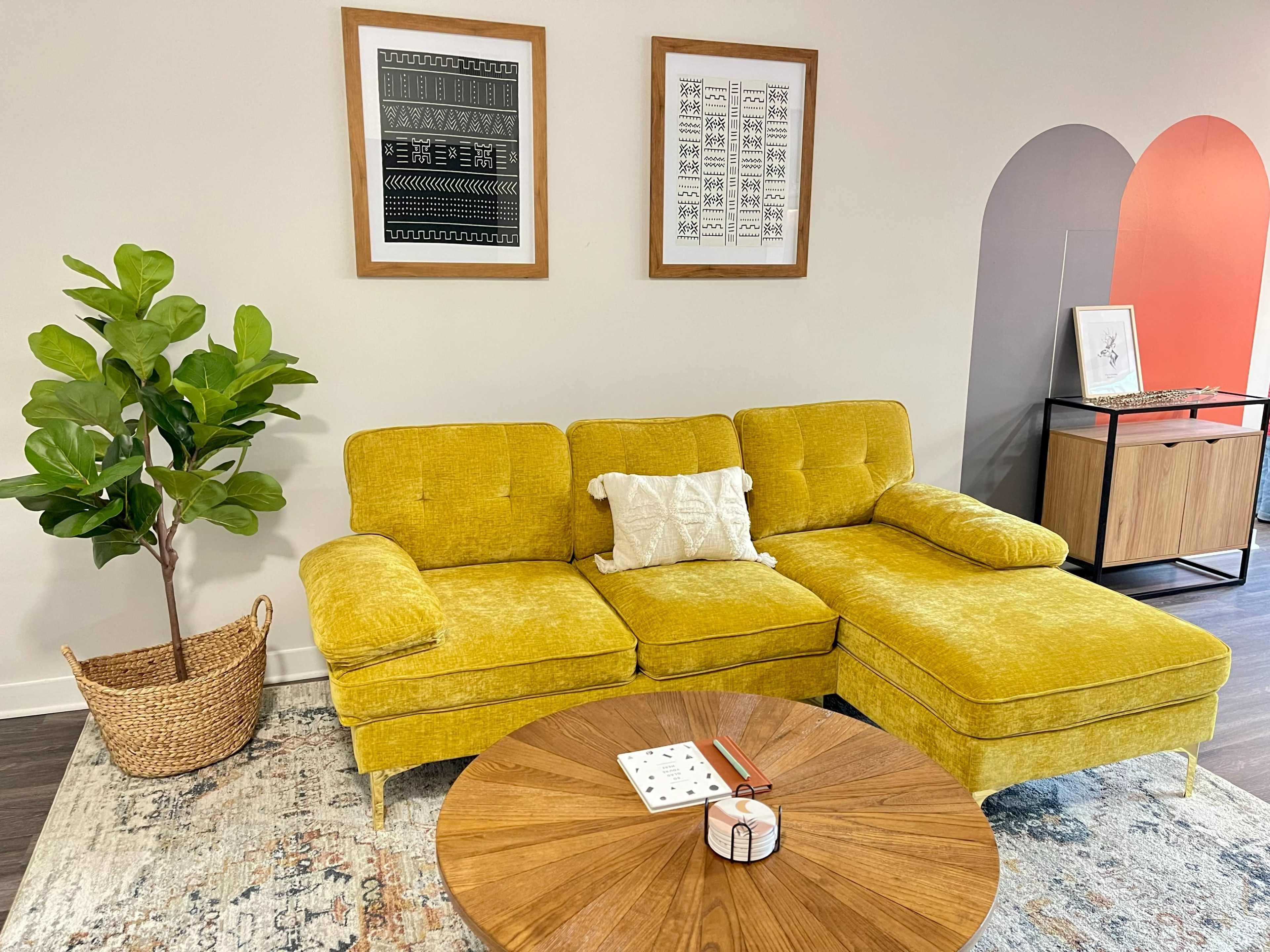 A yellow sectional sofa with a decorative pillow sits in a modern room, accompanied by a round wooden coffee table and a potted plant.