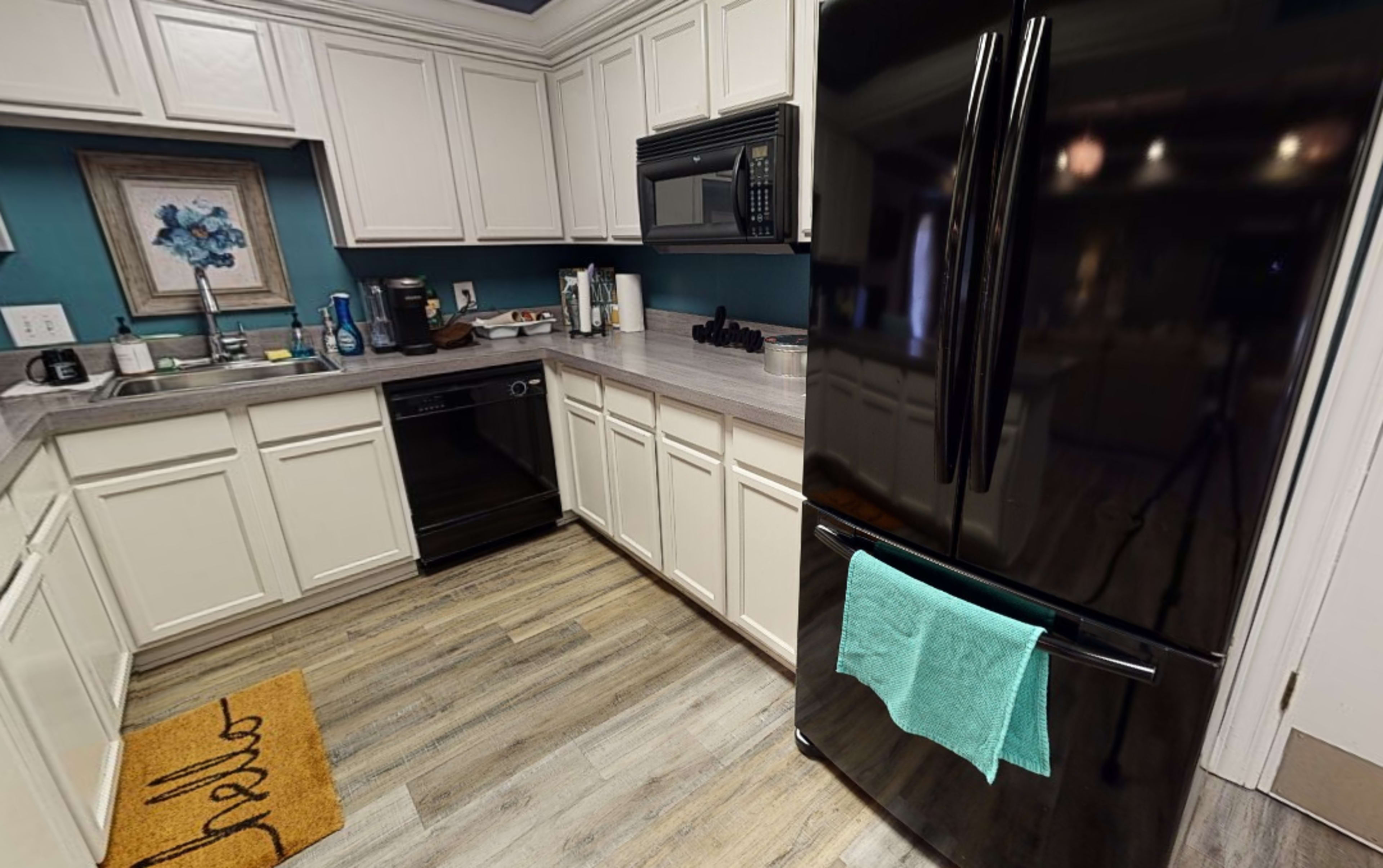 A modern kitchen features white cabinets, a black refrigerator, a black dishwasher, and a gray countertop with various kitchen items.