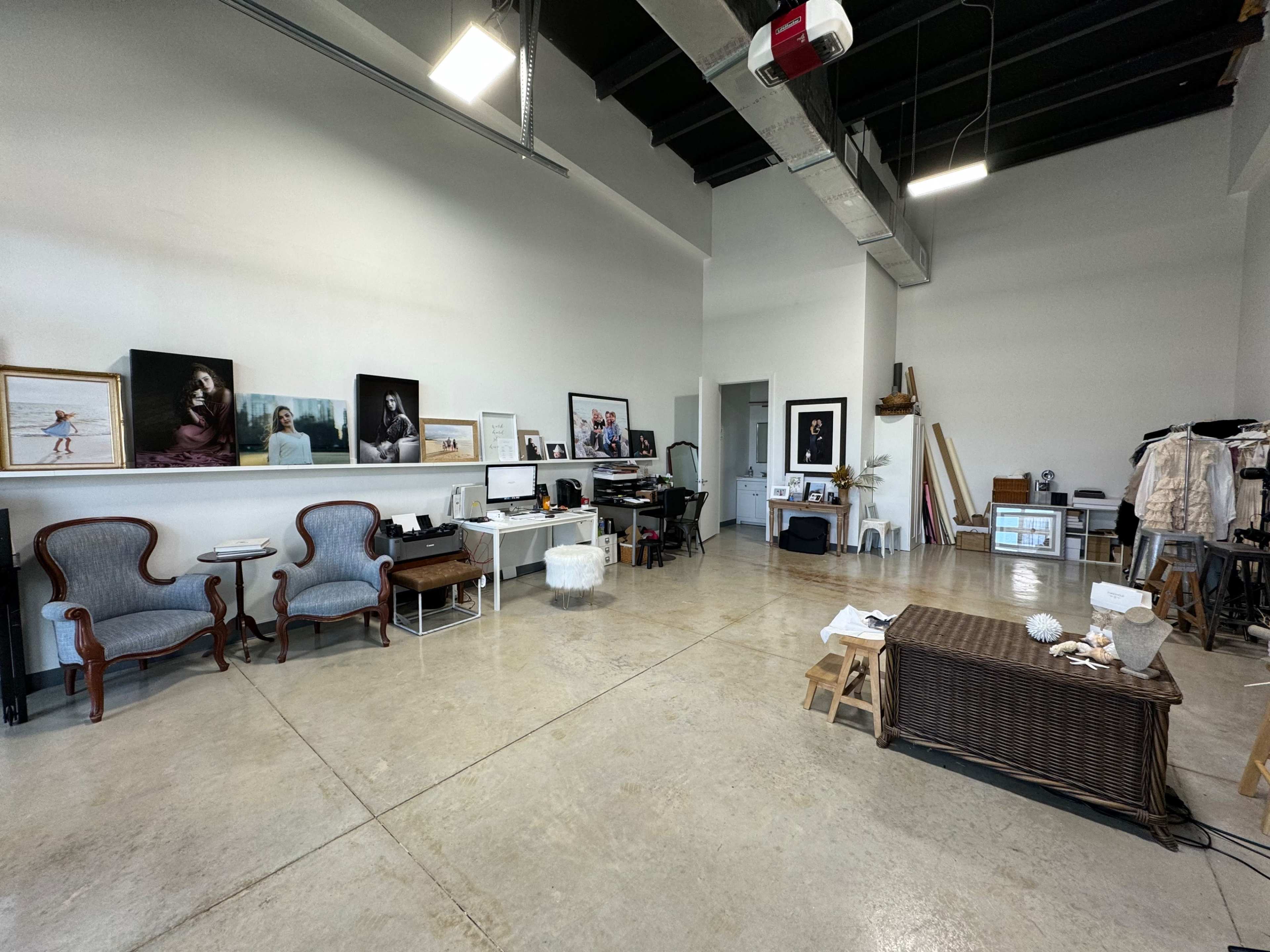 A spacious studio with concrete flooring, a desk, armchairs, framed artwork on the walls, and various furnishings arranged throughout.