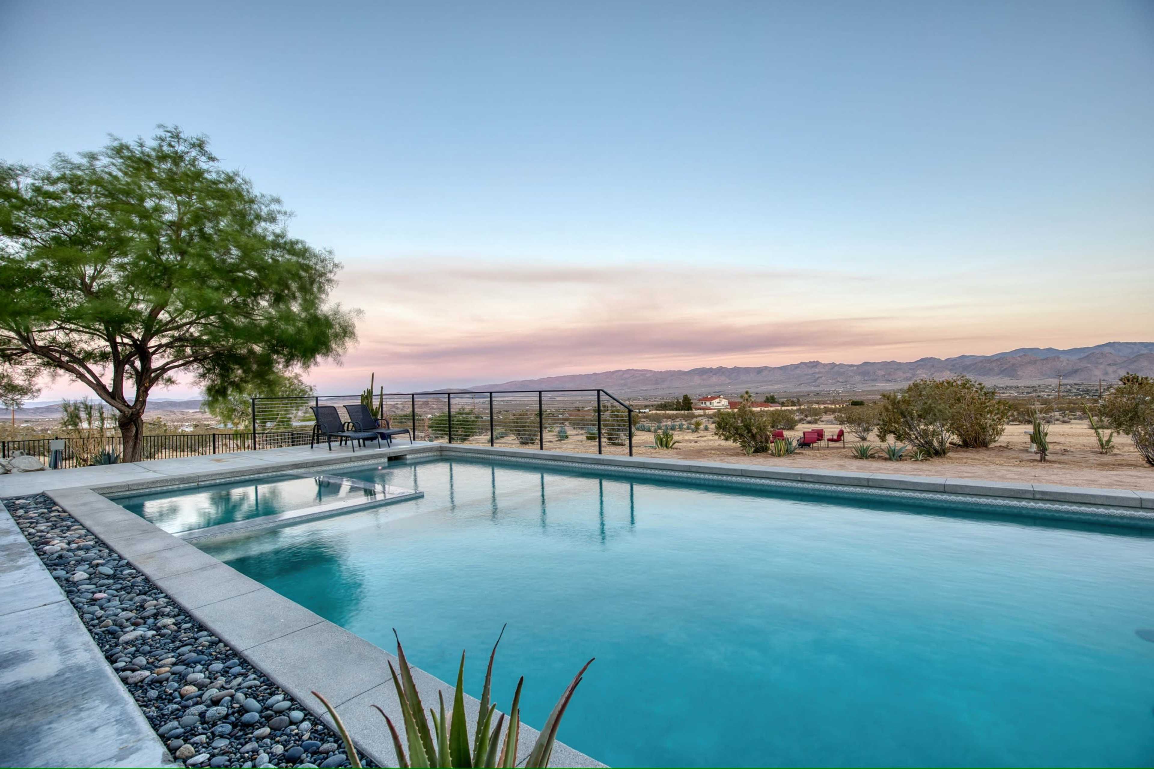 The image shows a swimming pool with a desert landscape and mountains in the background under a clear sky.