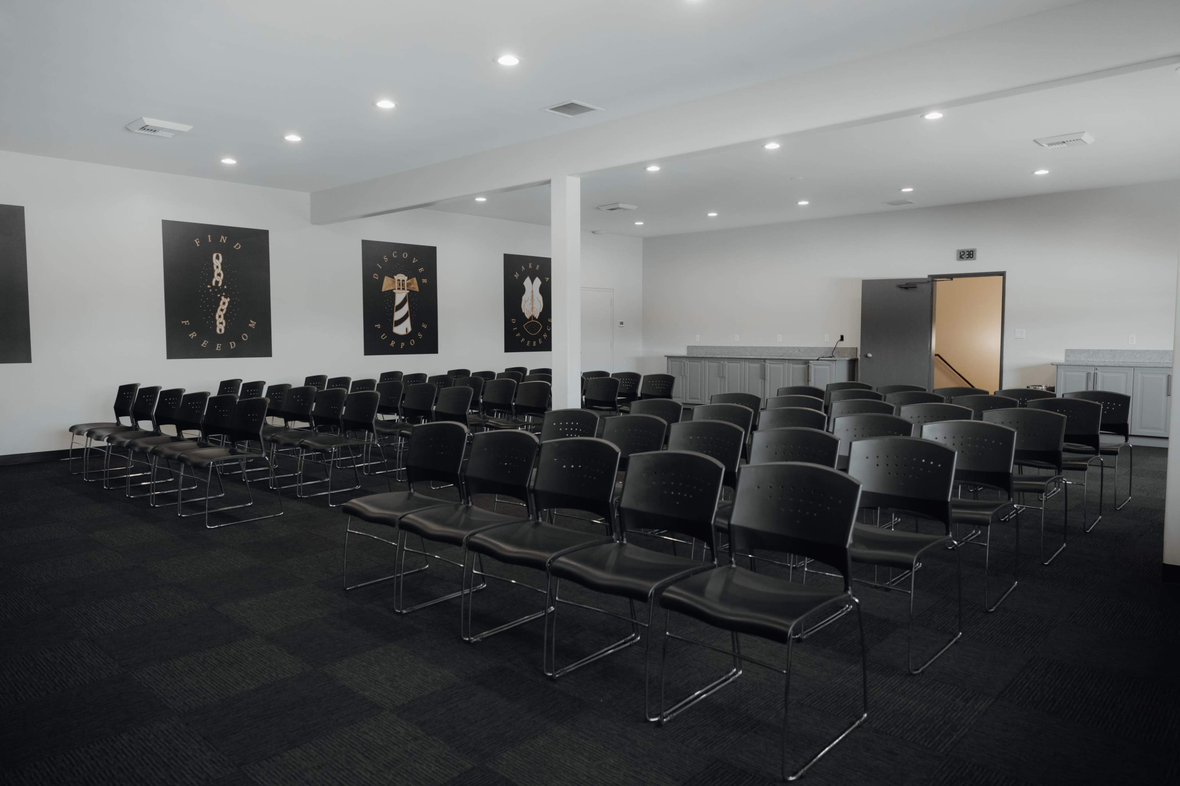 A row of black chairs arranged in a meeting room with artwork displayed on the walls.